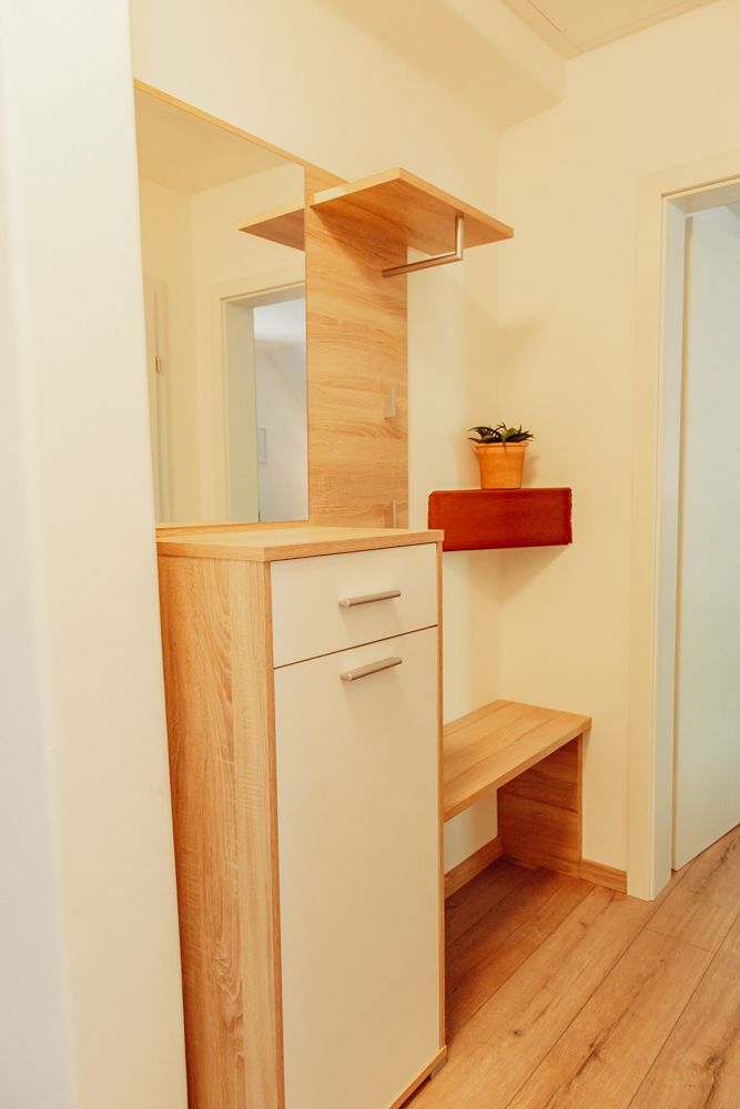 Modern előszoba, fából készült szekrénnyel, tükörrel és növényekkel.