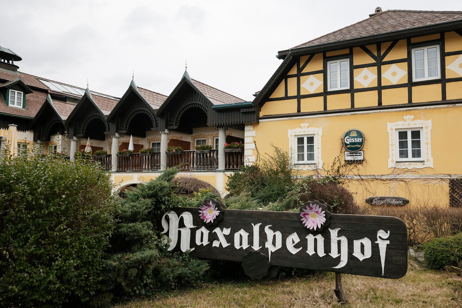 Hagyományos vendéglő sárga homlokzattal és fából készült verandákkal, amely előtt a "Raxalpenhof" felirat olvasható.