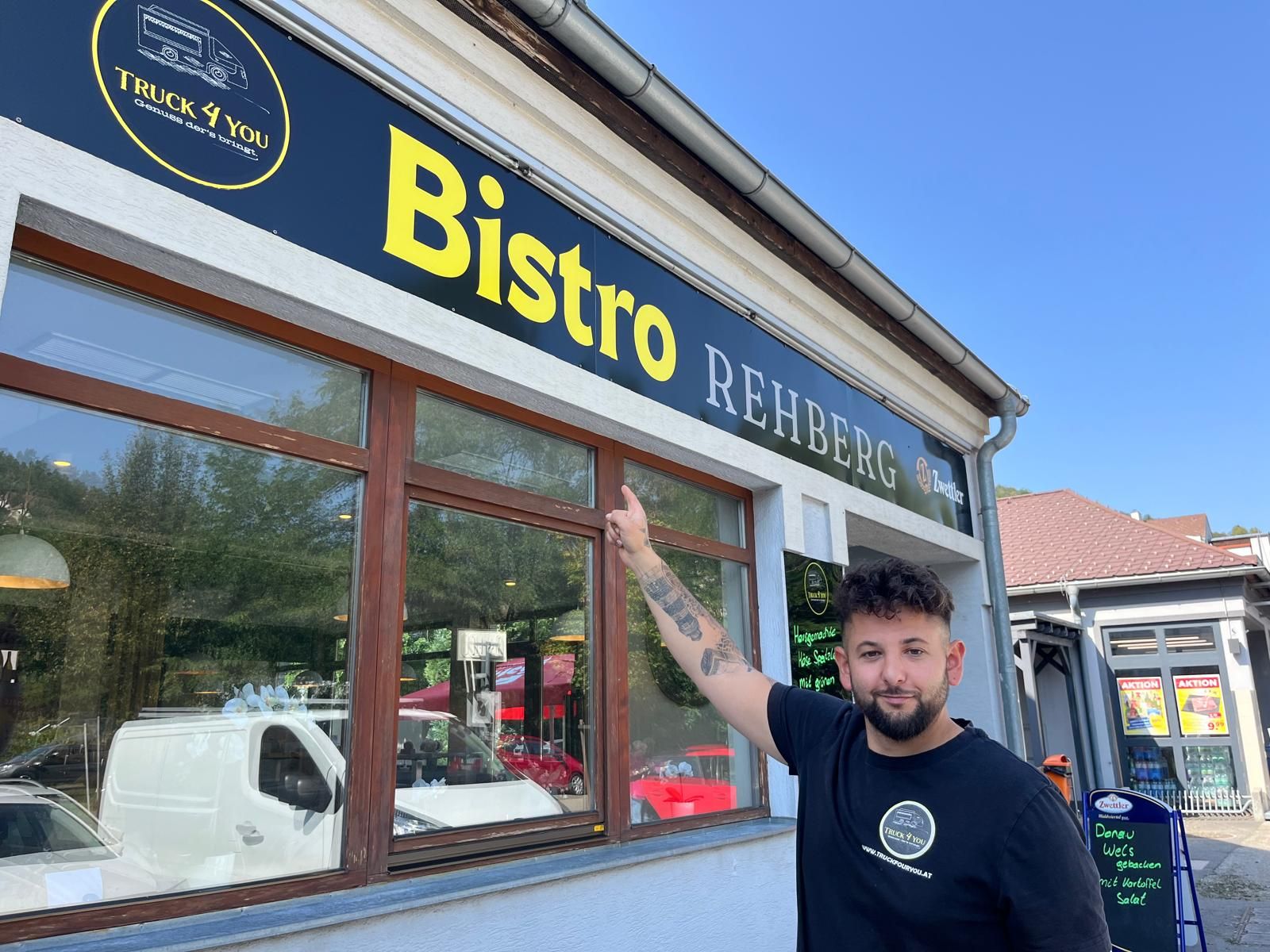 Egy férfi rámutat egy táblára, amelyen az áll: "Bistro Rehberg".