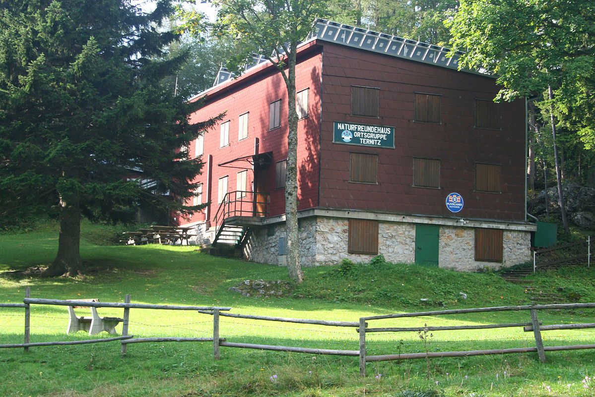 Piros színű, faburkolatos épület, fákkal és réttel körülvéve, "Naturfreundehaus Ortsgruppe Ternitz" felirattal.