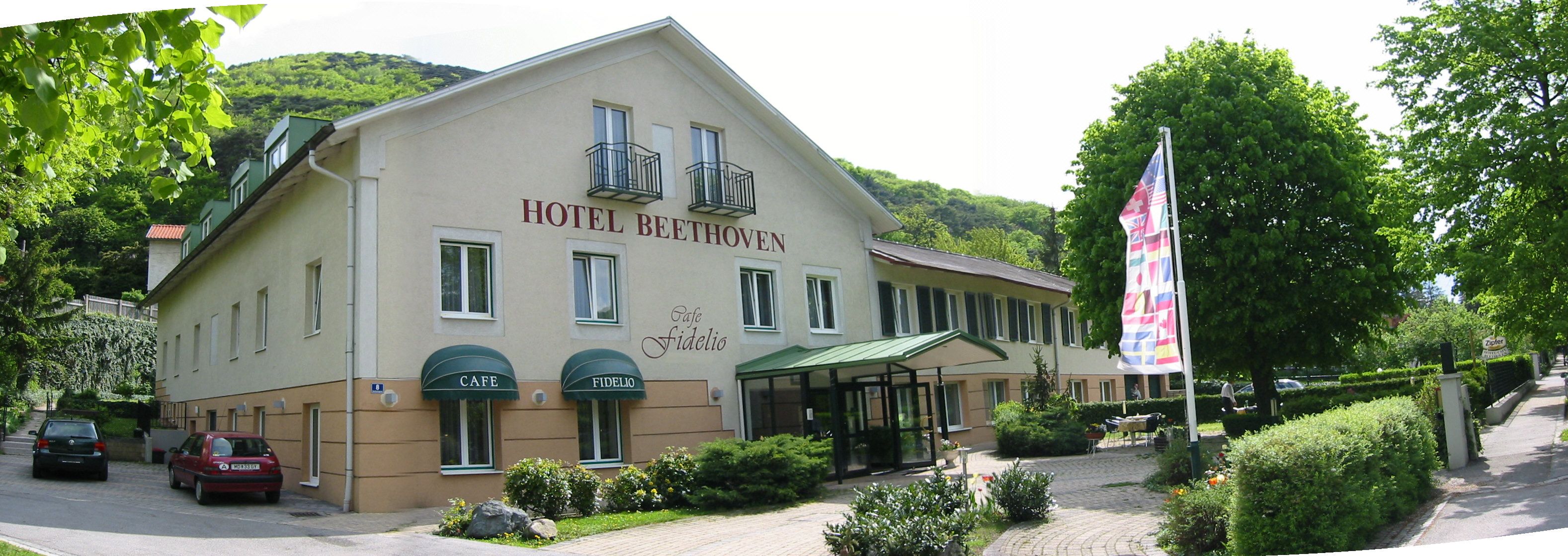 A Hotel Beethoven külső nézete a Café Fidelióval, fákkal és zászlókkal körülvéve.