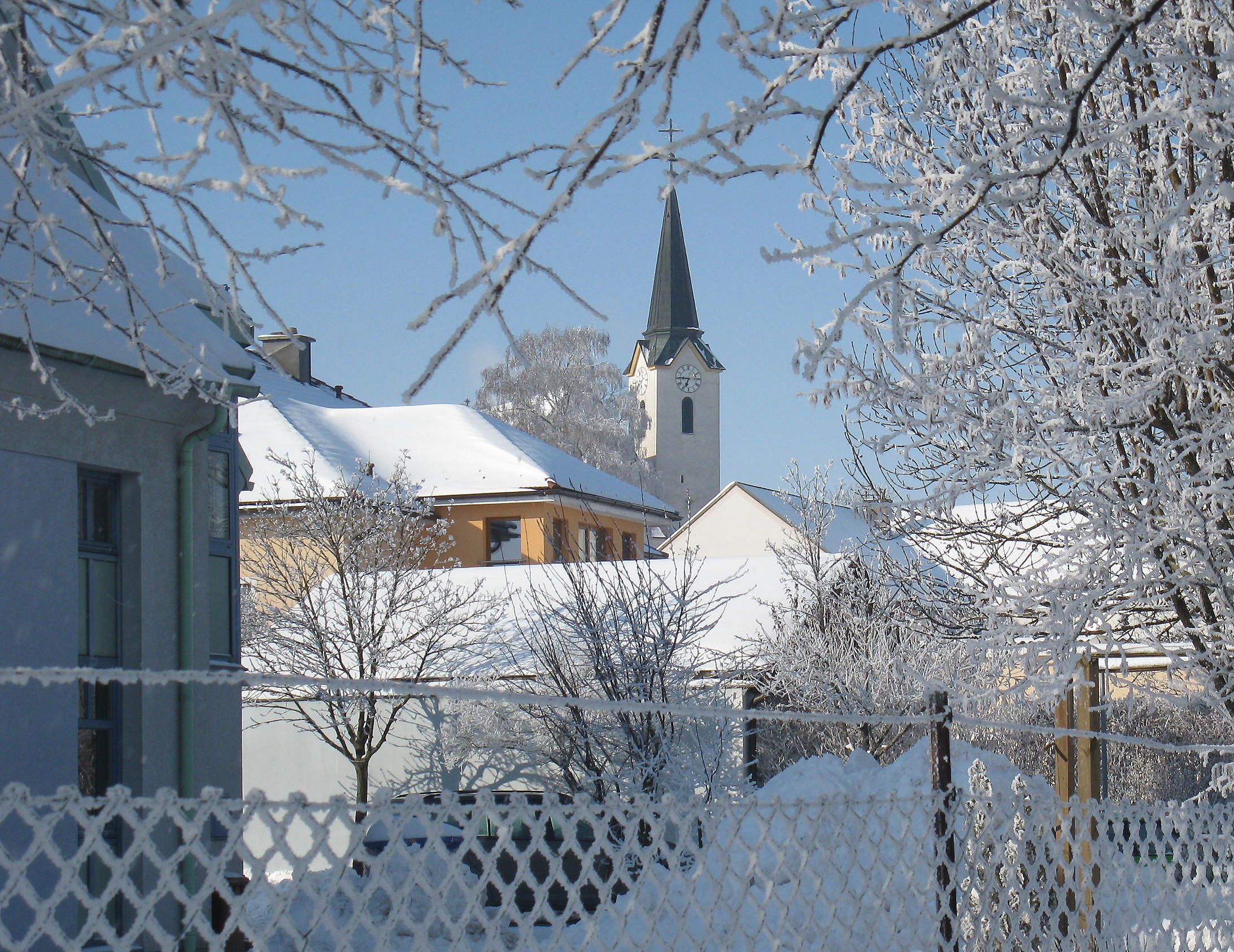 Hófödte falu látképe templommal és fákkal télen.