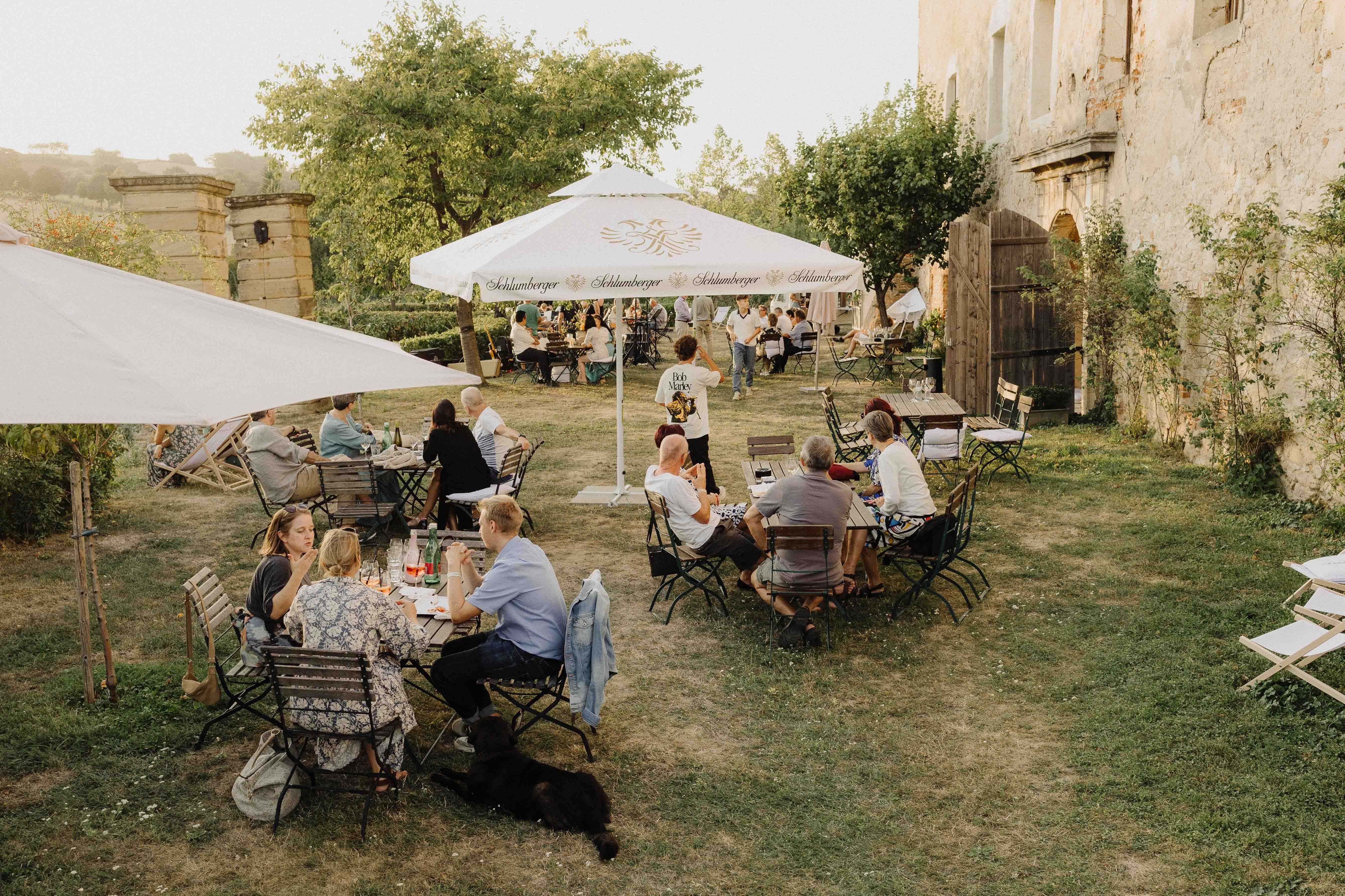 Az emberek szabadtéri asztaloknál ülnek a kertben, napernyőkkel.
