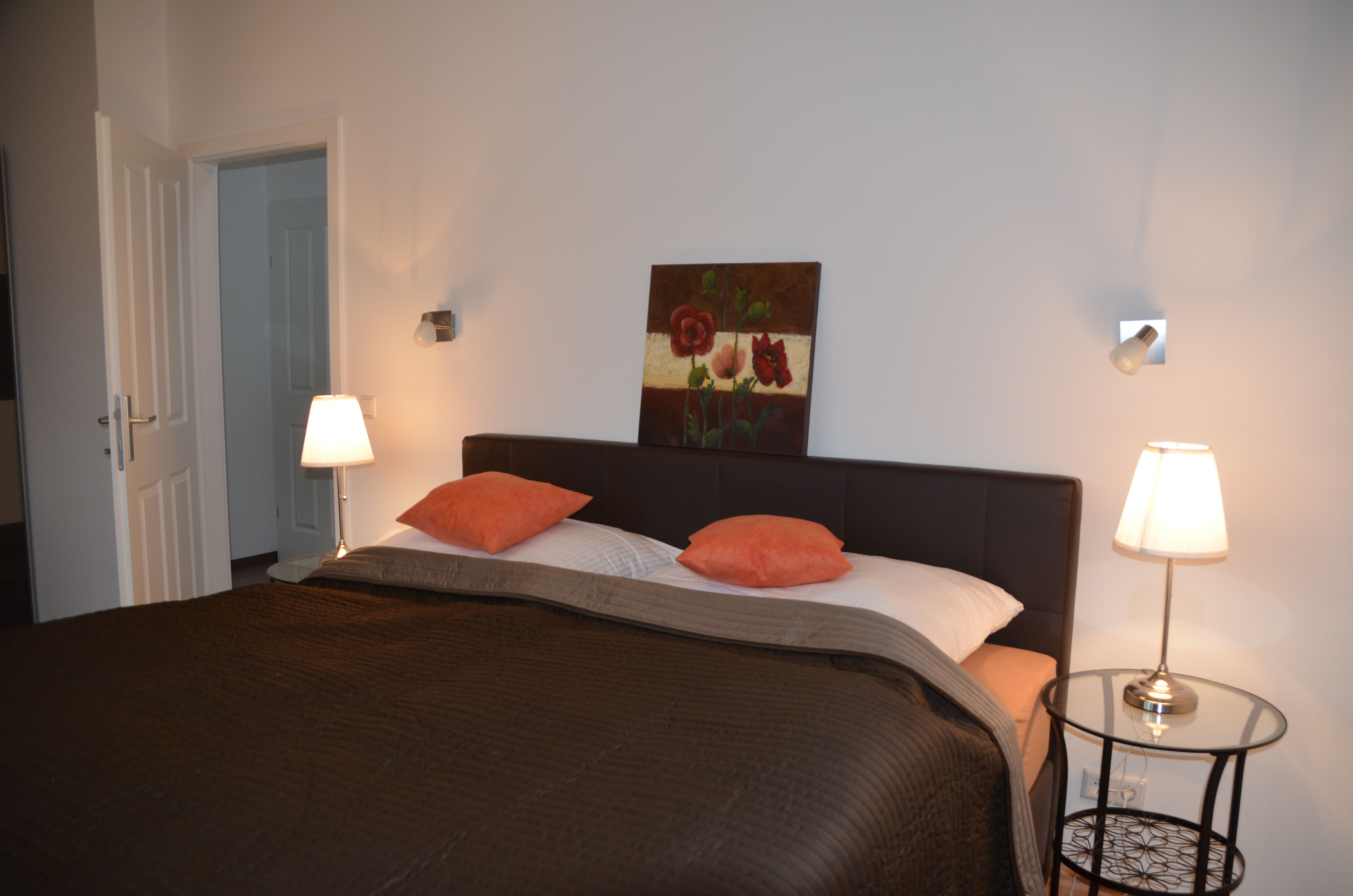 Hálószoba franciaággyal, két éjjeli lámpával és egy festménnyel a falon.