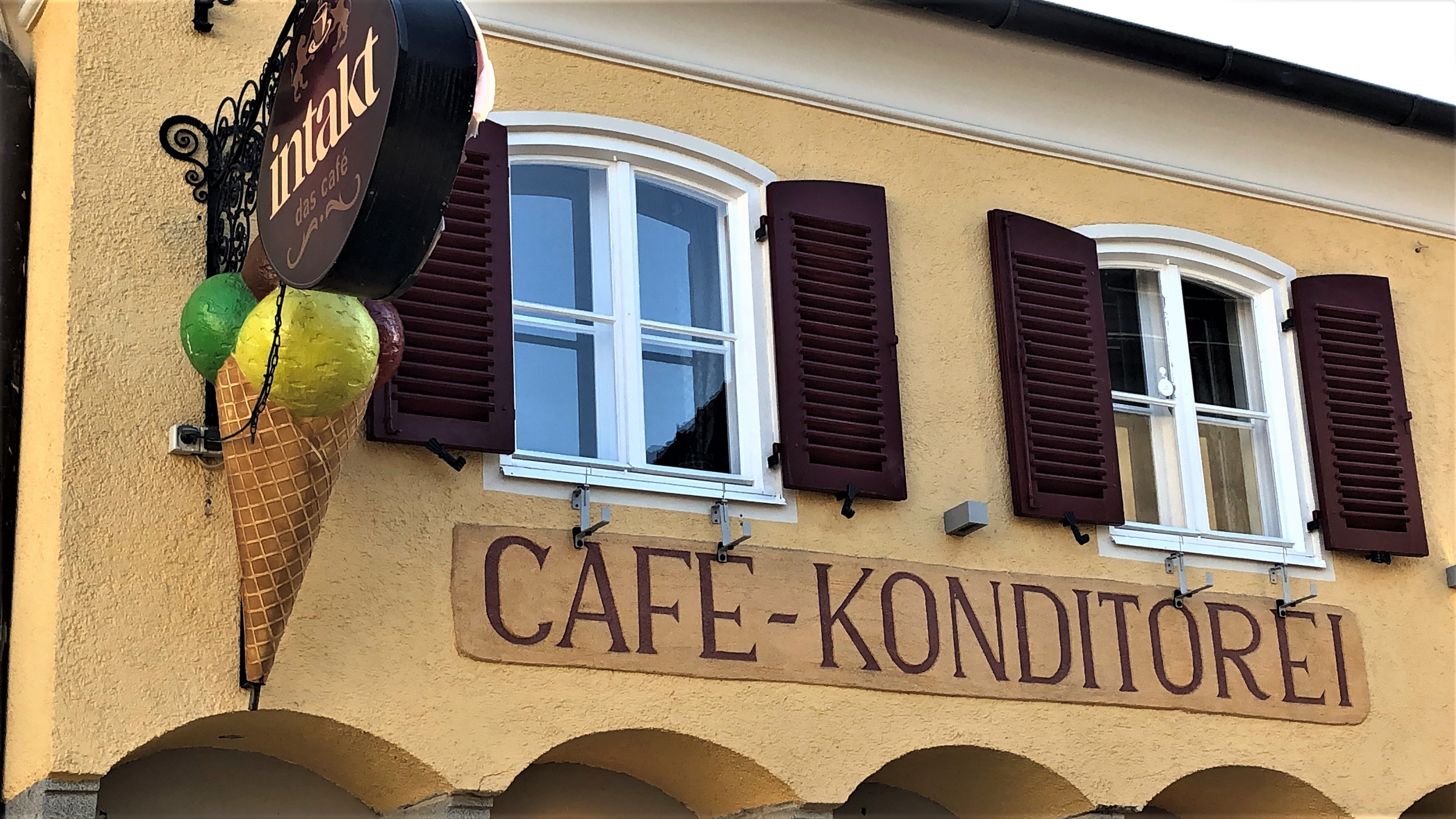 Egy kávézó homlokzata fagylaltkúp díszítéssel és "Cafe-Konditorei" felirattal.