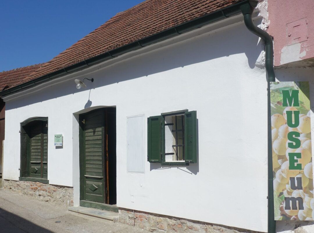 Fehér épület zöld redőnyökkel és ajtóval, felirat: "MÚZEUM".