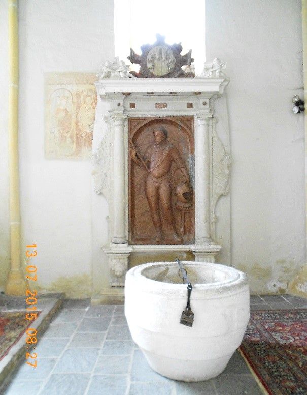 Sír domborművel és keresztelőmedencével egy templomban.