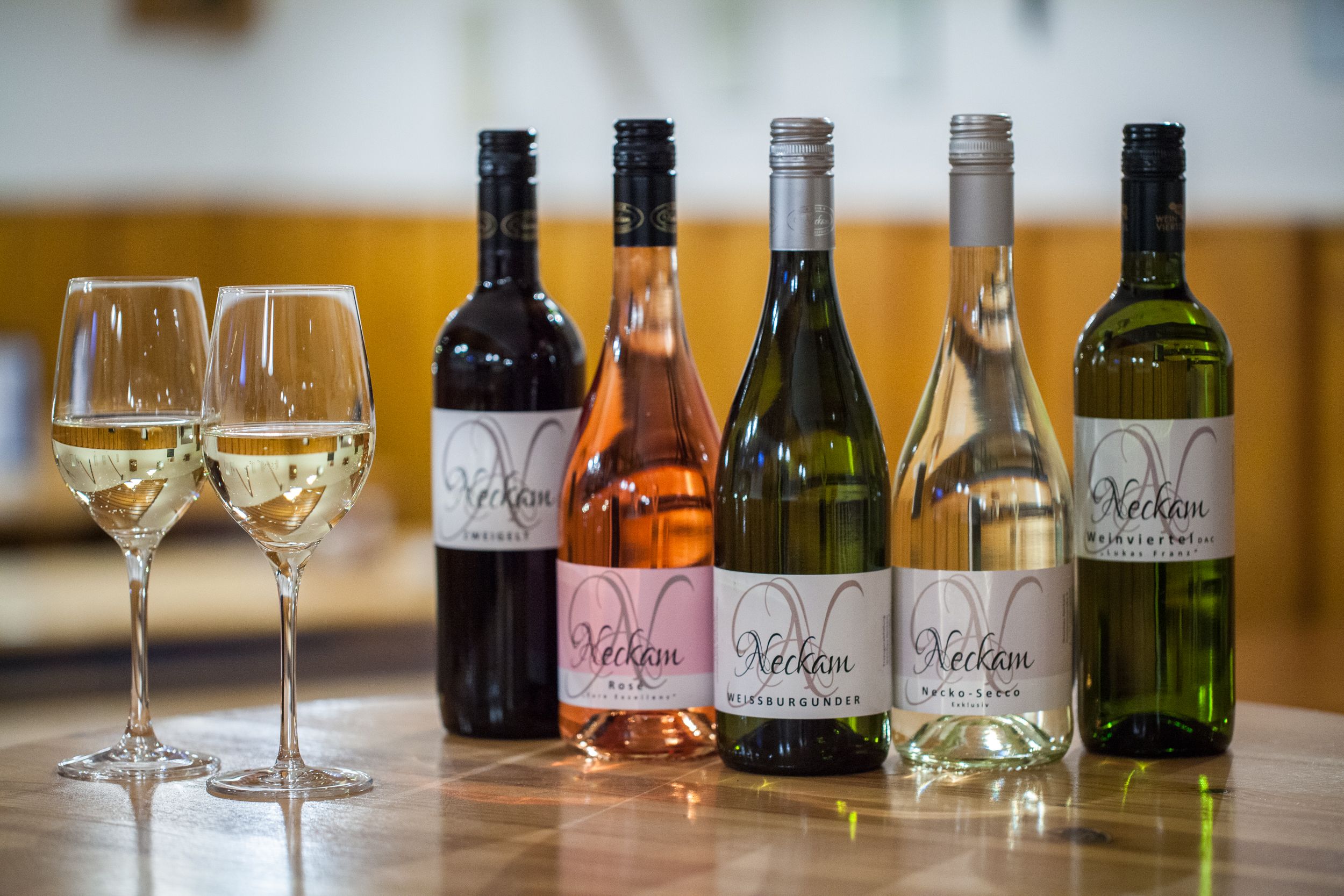 Öt üveg bor és két teli borospohár egy faasztalon.