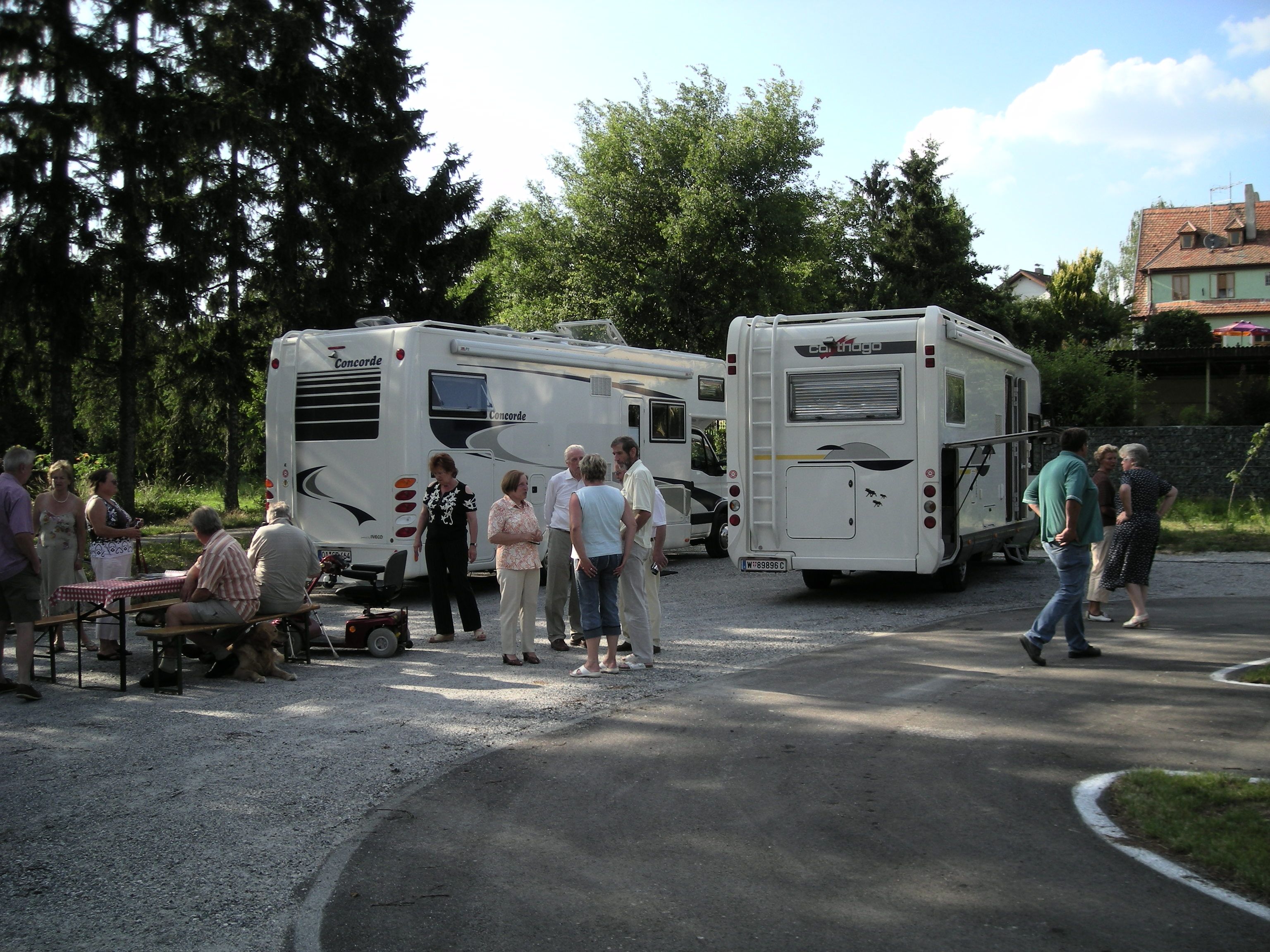 Az emberek két mobilház mellett állnak és ülnek egy szabadtéri pályán.