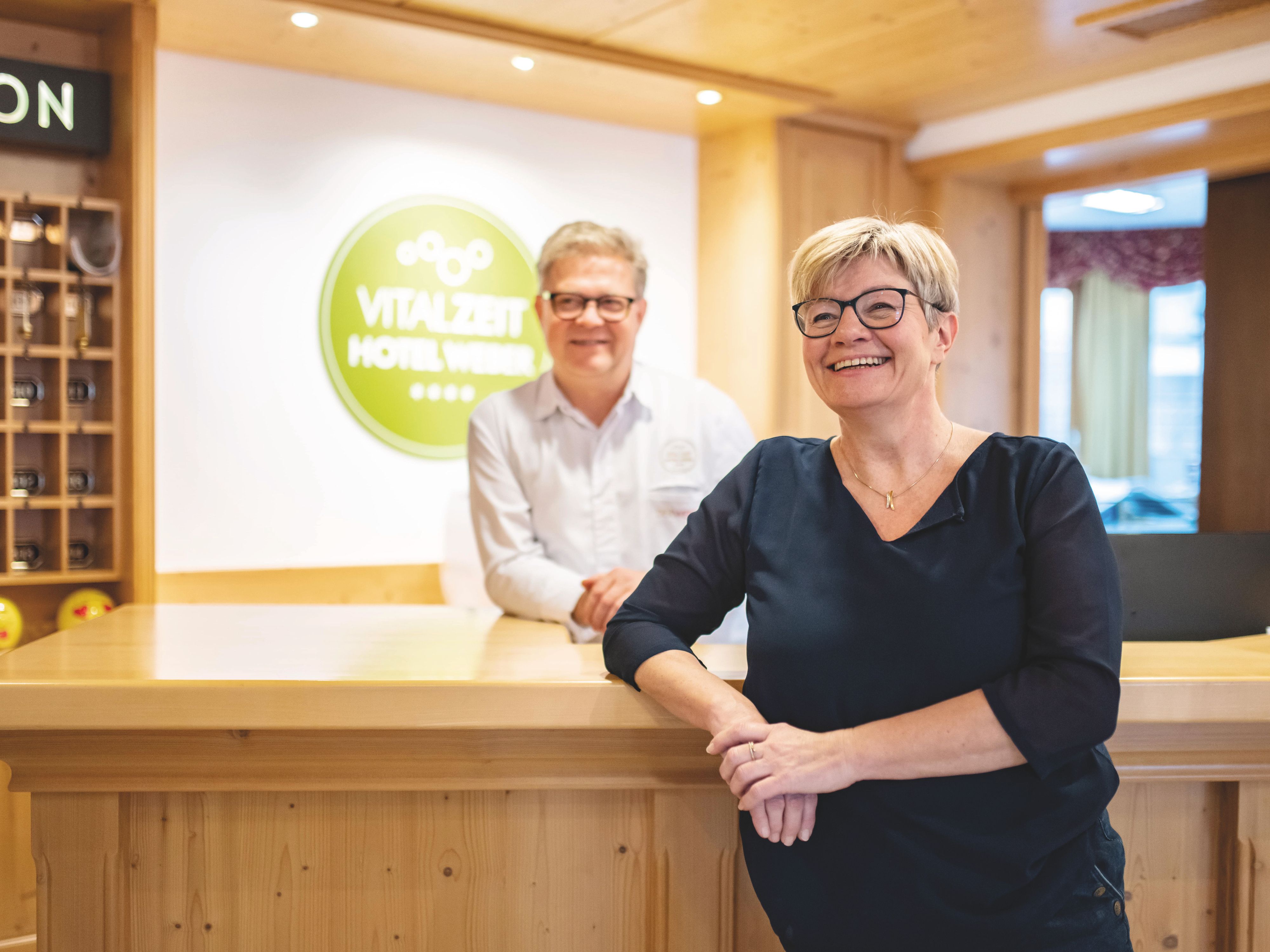 Petra és Alfred Weber mosolyogva állnak a VitalZeit Hotel Weber recepcióján.