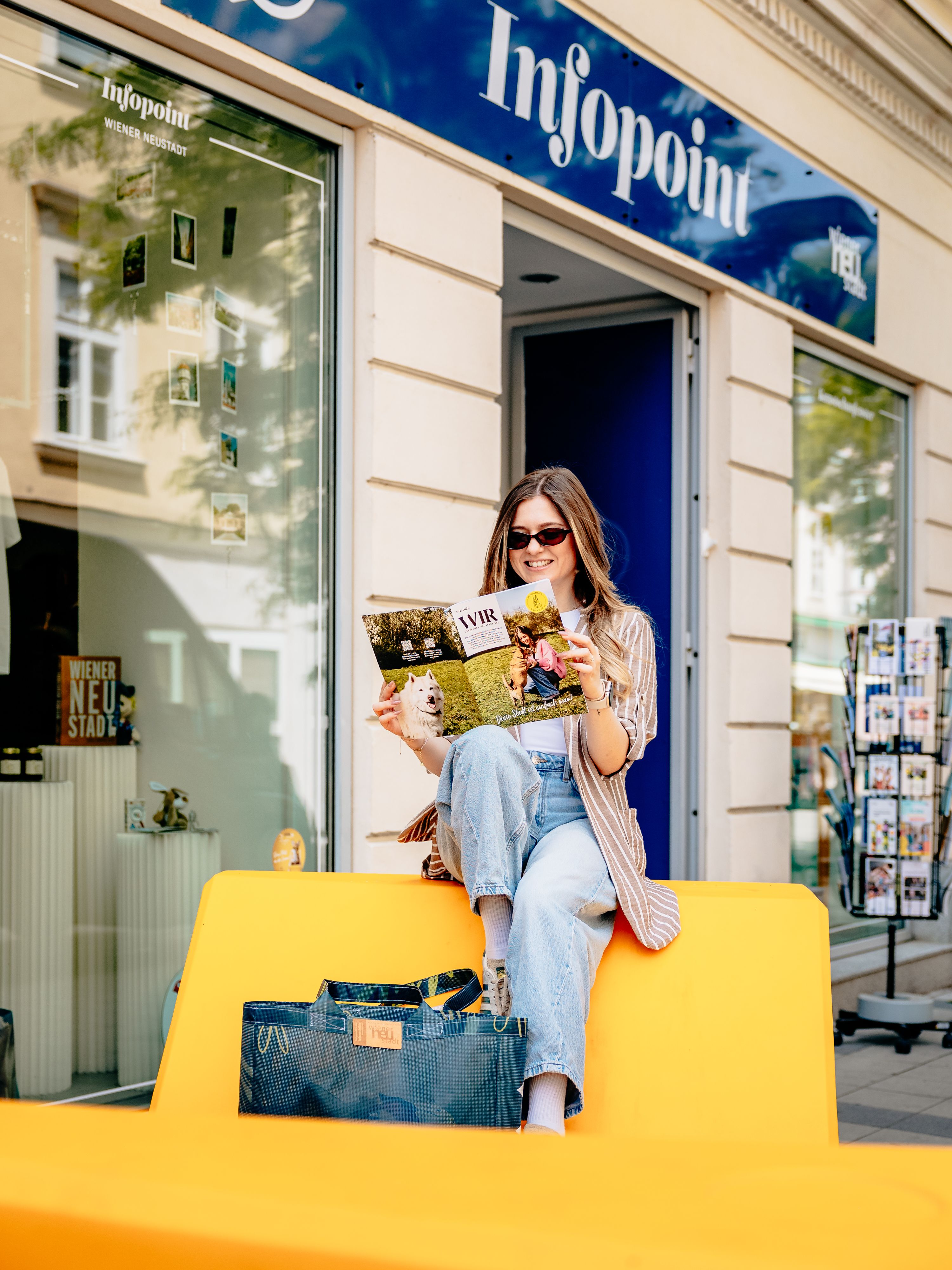 Színes Enzi-figurák az Infopoint előtt, ahol egy nő a város magazinját olvassa