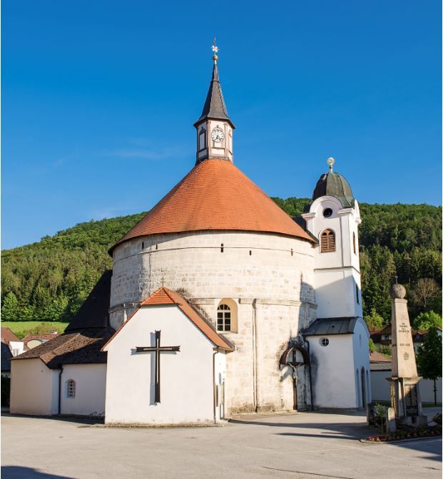Scheiblingkircheni plébániatemplom kerek toronnyal és vörös tetővel a kék égbolton.