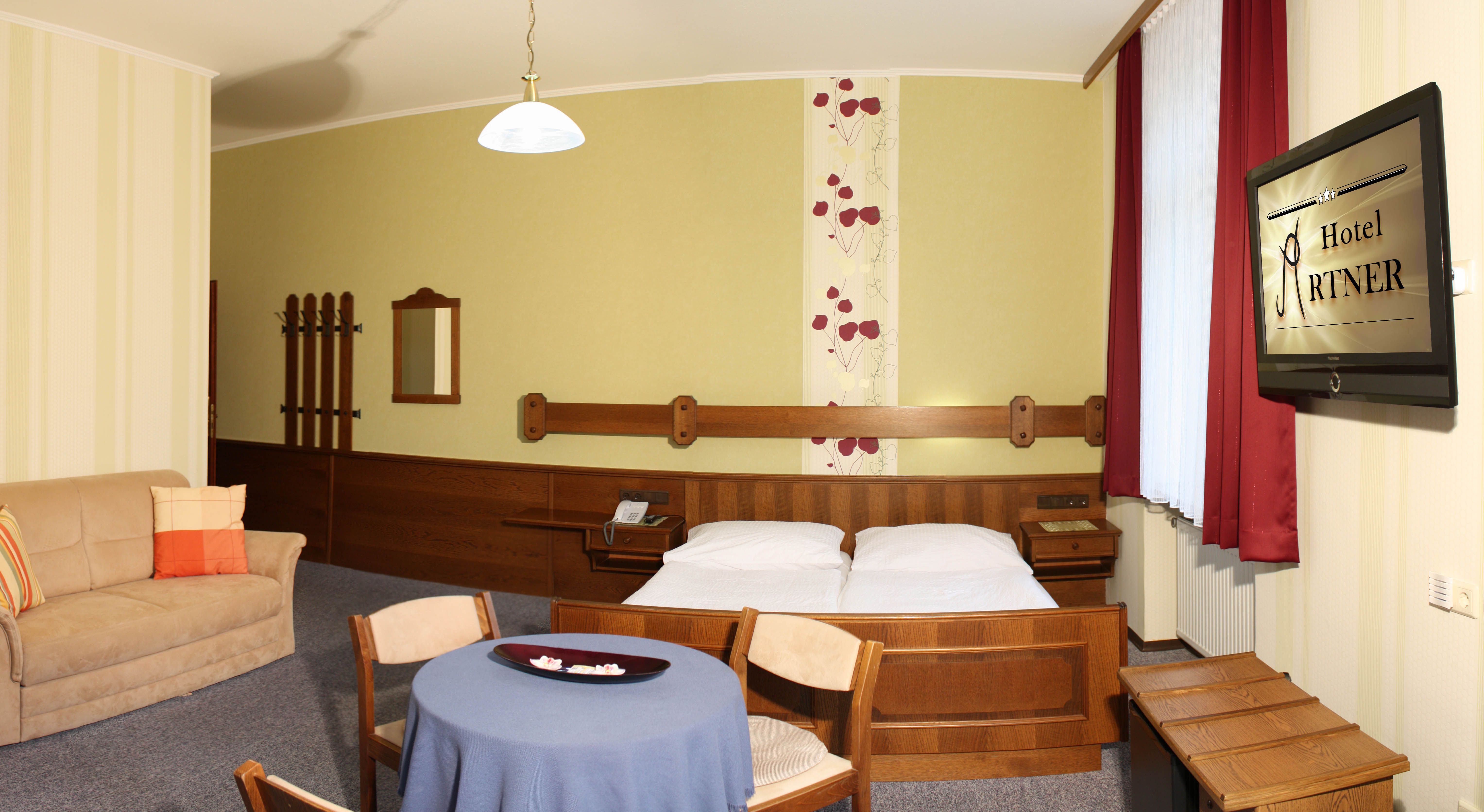 Hotelszoba franciaággyal, kanapéval, asztallal és televízióval.