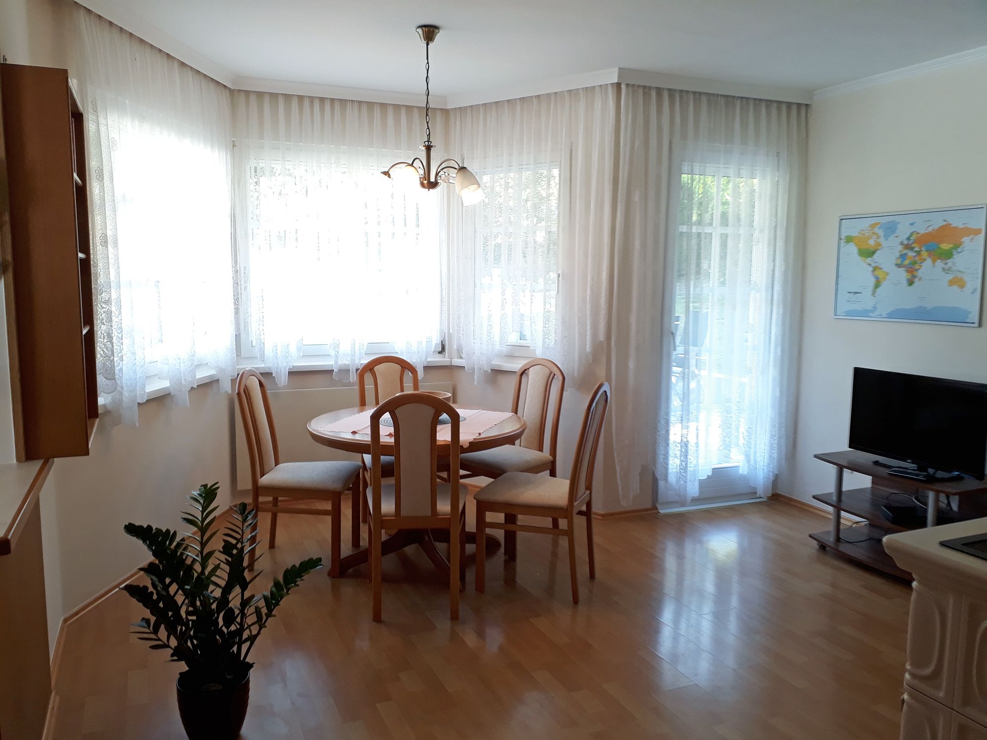 Világos étkezős konyha étkezőasztallal, székekkel, TV-vel és világtérképpel a falon.