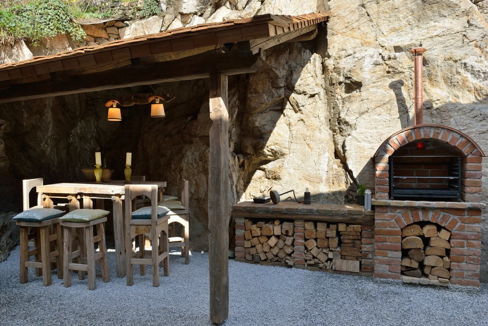 Rusztikus szabadtéri terület fa asztallal, székekkel és tégla sütővel.