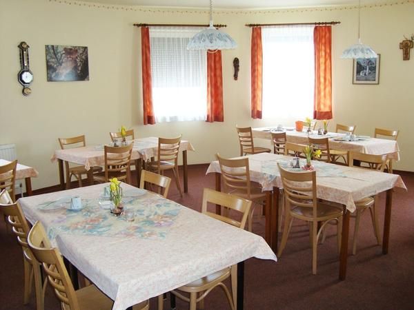 Hangulatos reggelizőterem, több terített asztallal és fából készült székekkel, virágokkal és képekkel díszített falakkal.