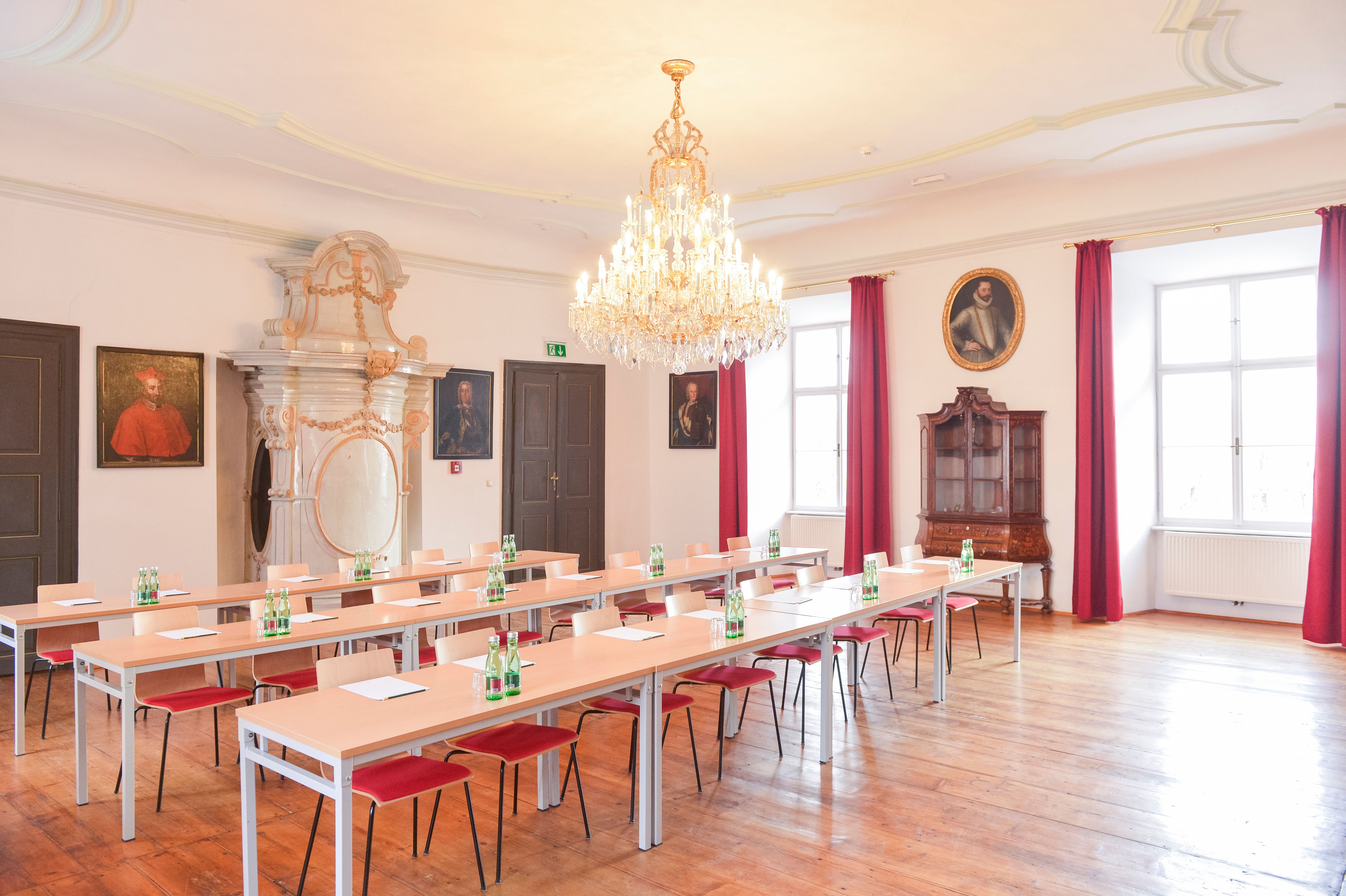 Elegáns szemináriumi terem csillárral, fapadlóval és portrékkal a falakon.