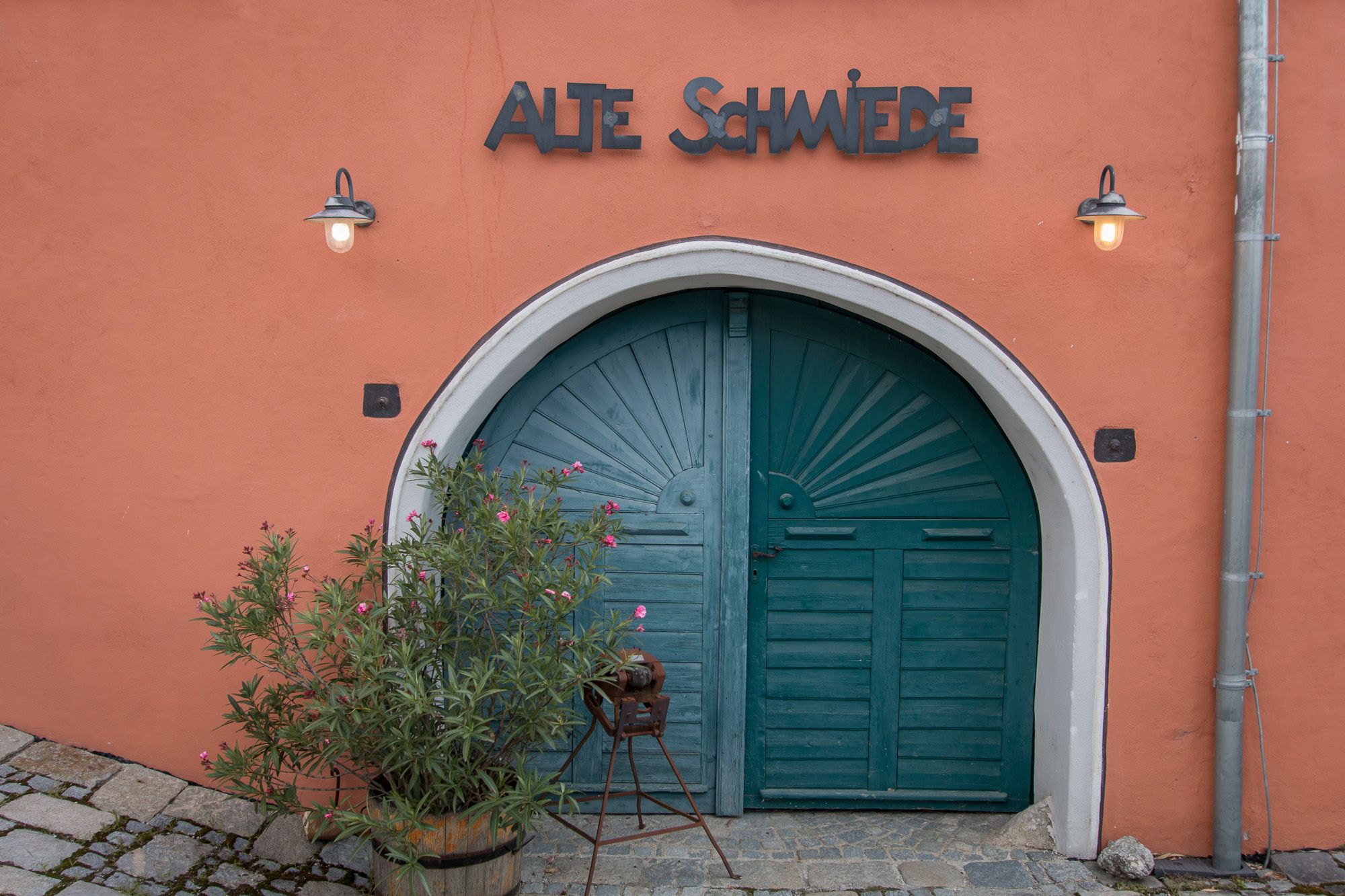 Régi kapu "Alte Schmiede" felirattal és növényekkel előtte.