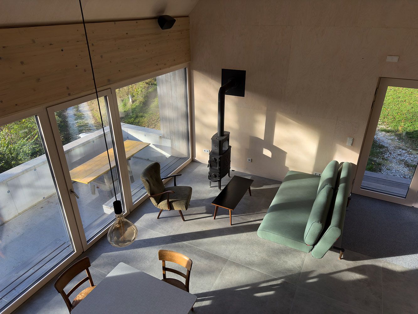 Modern nappali és étkező nagy ablakokkal, kanapéval, fotelekkel és kandallóval.