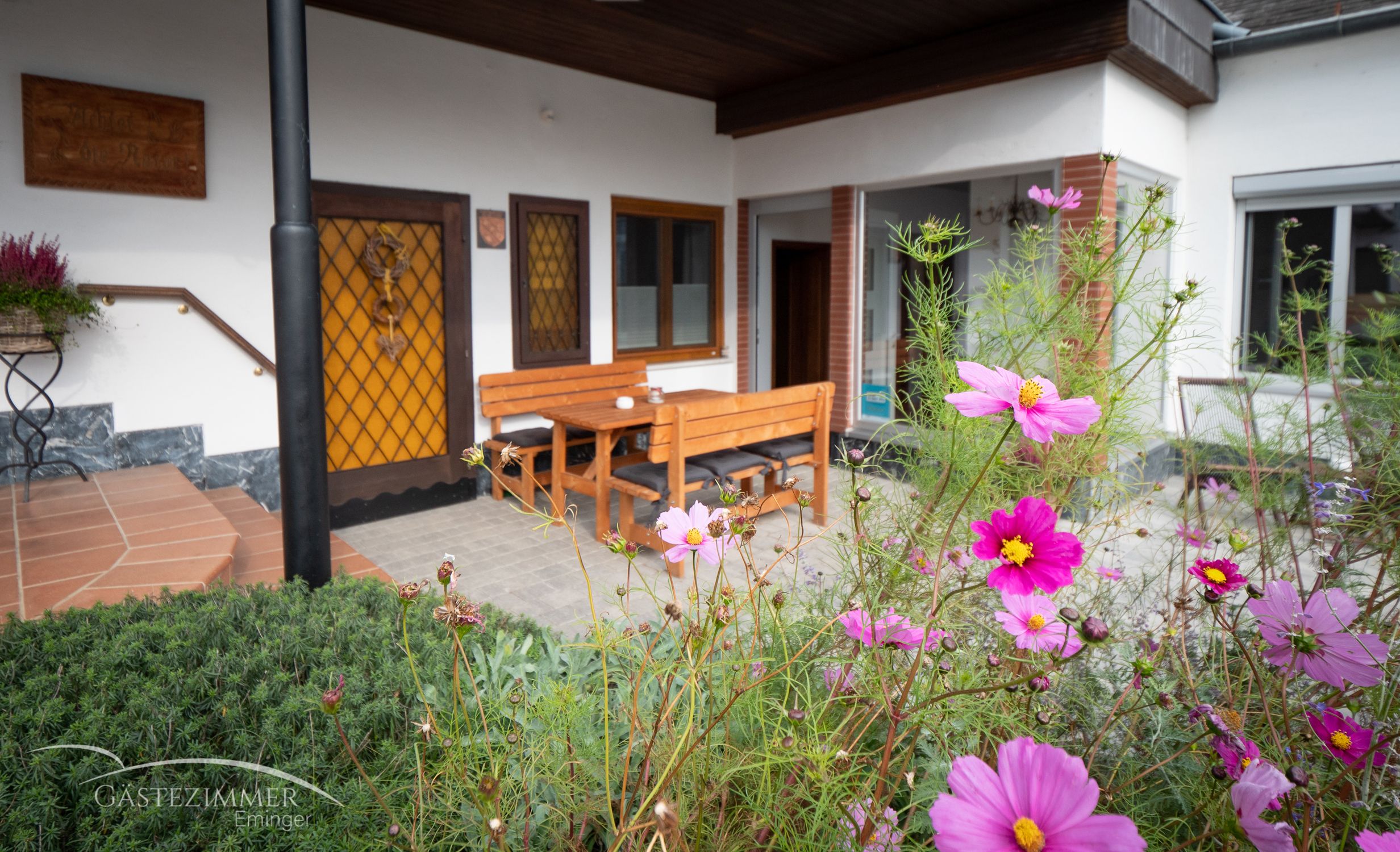 Terasz fából készült bútorokkal és virágzó virágokkal az előtérben.