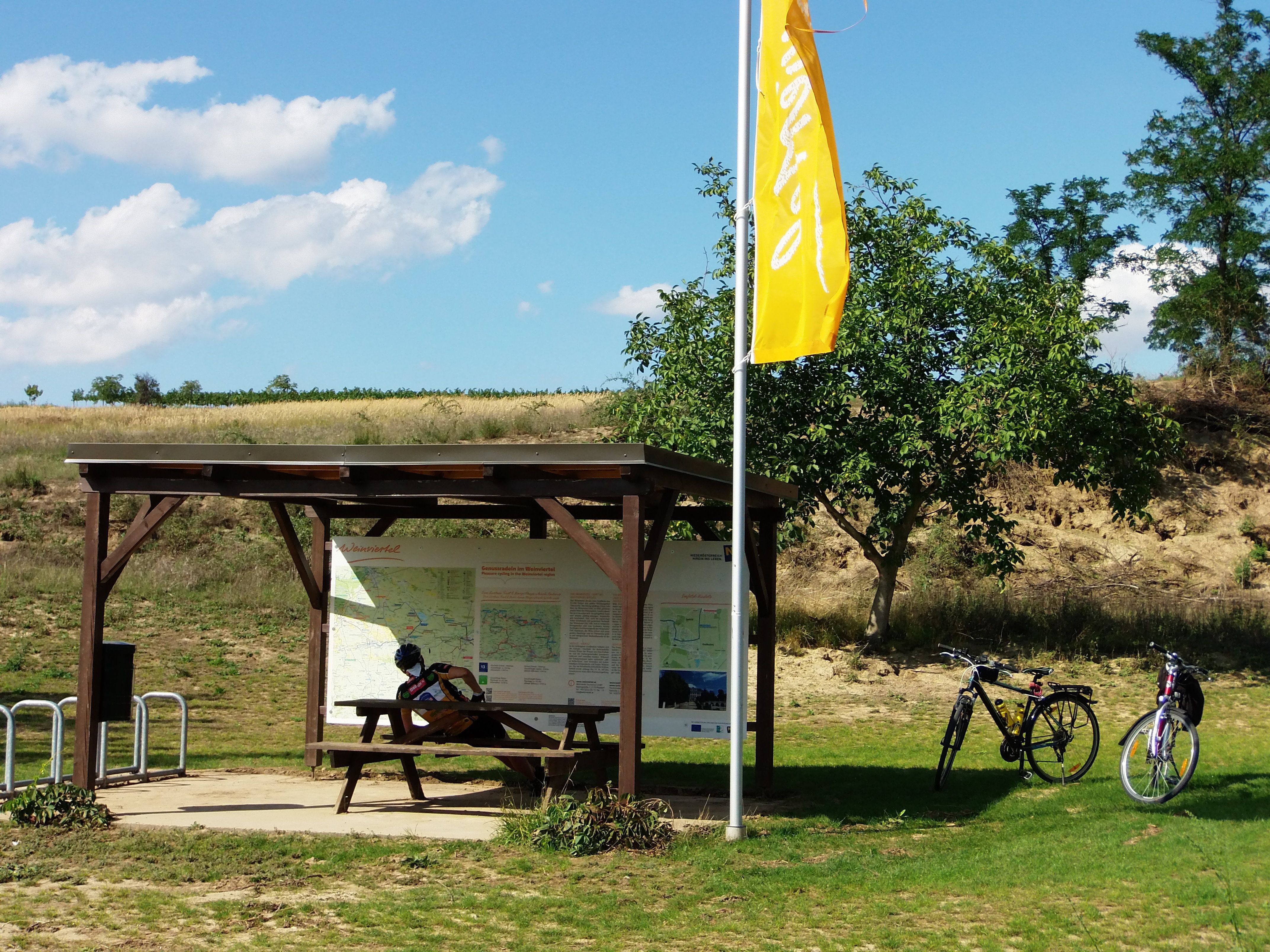 Kerékpárosok pihenőhelye faasztallal, két kerékpárral és információs táblával a Weinviertelben.