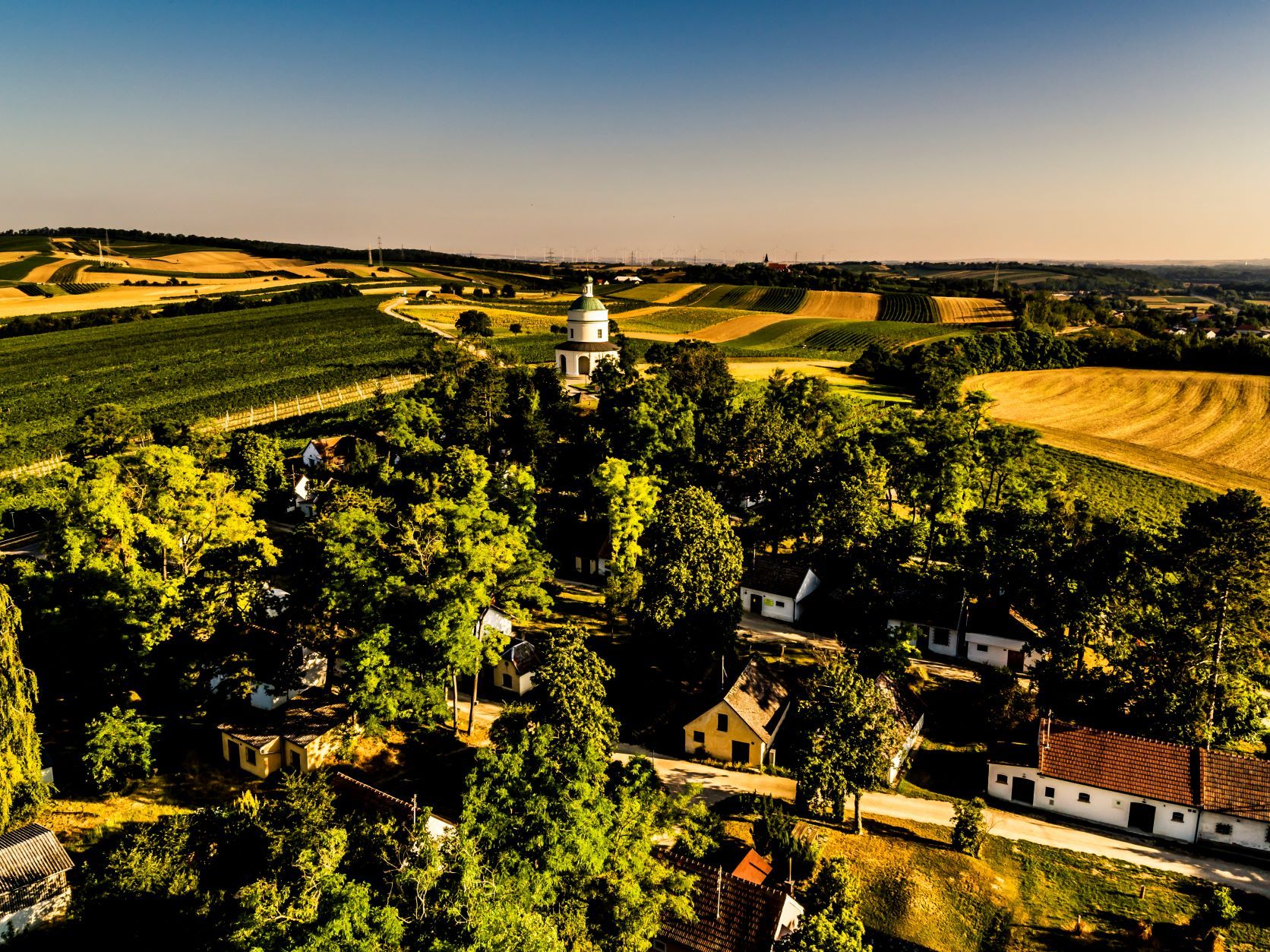 Tájkép mezőkkel, fákkal és egy kis templommal a közepén.
