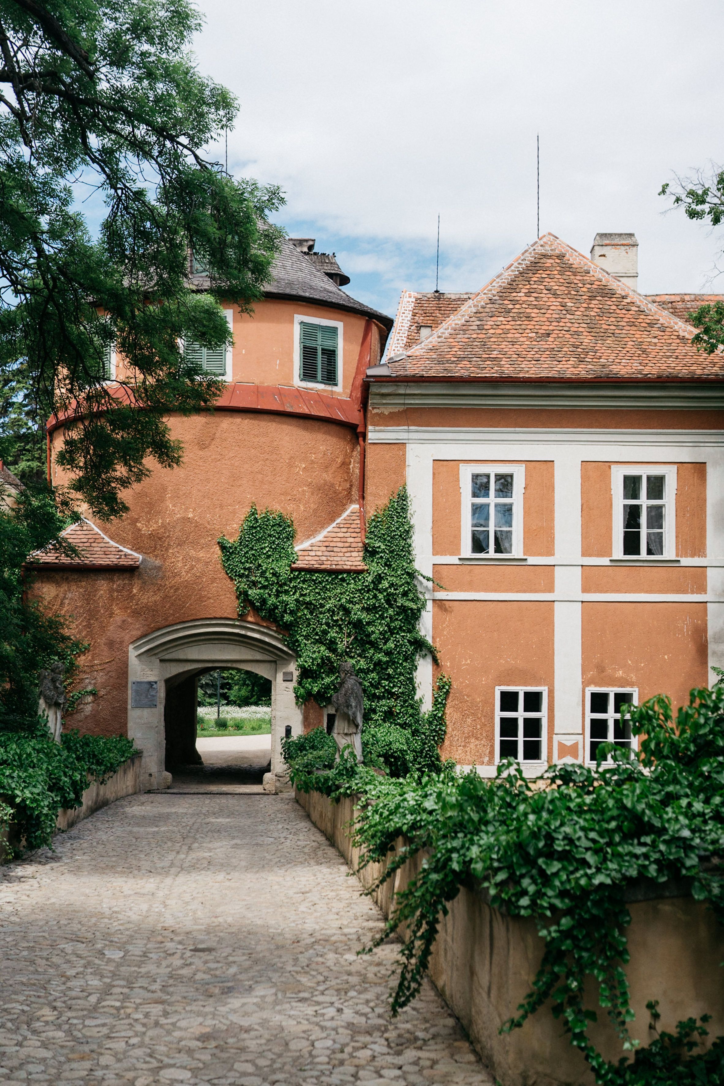 A Schrattenthal-kastély bejárati kapuja, benőtt homlokzattal és kövezett úttal.