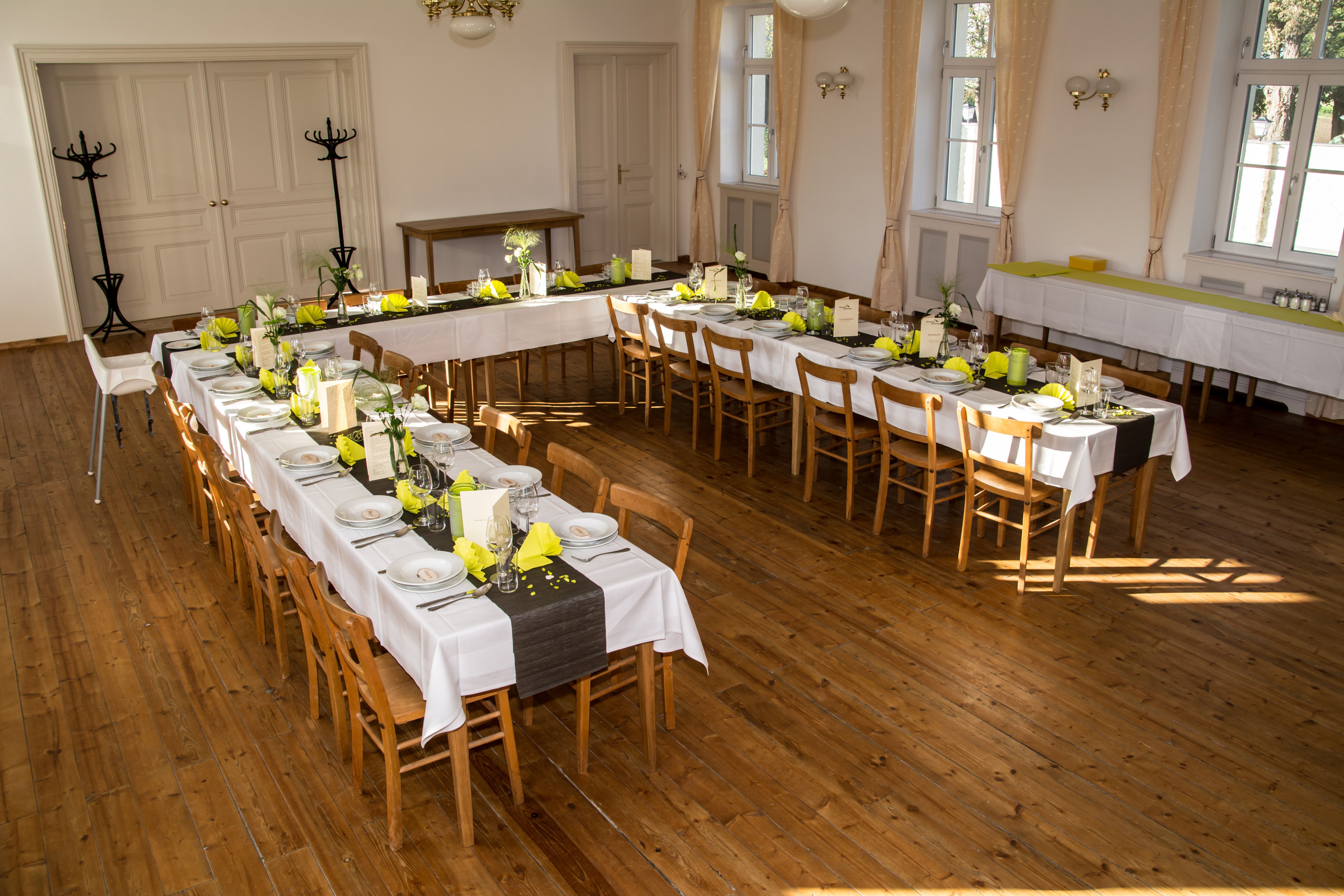 Ünnepélyesen díszített rendezvényterem hosszú asztalokkal és sárga szalvétákkal.