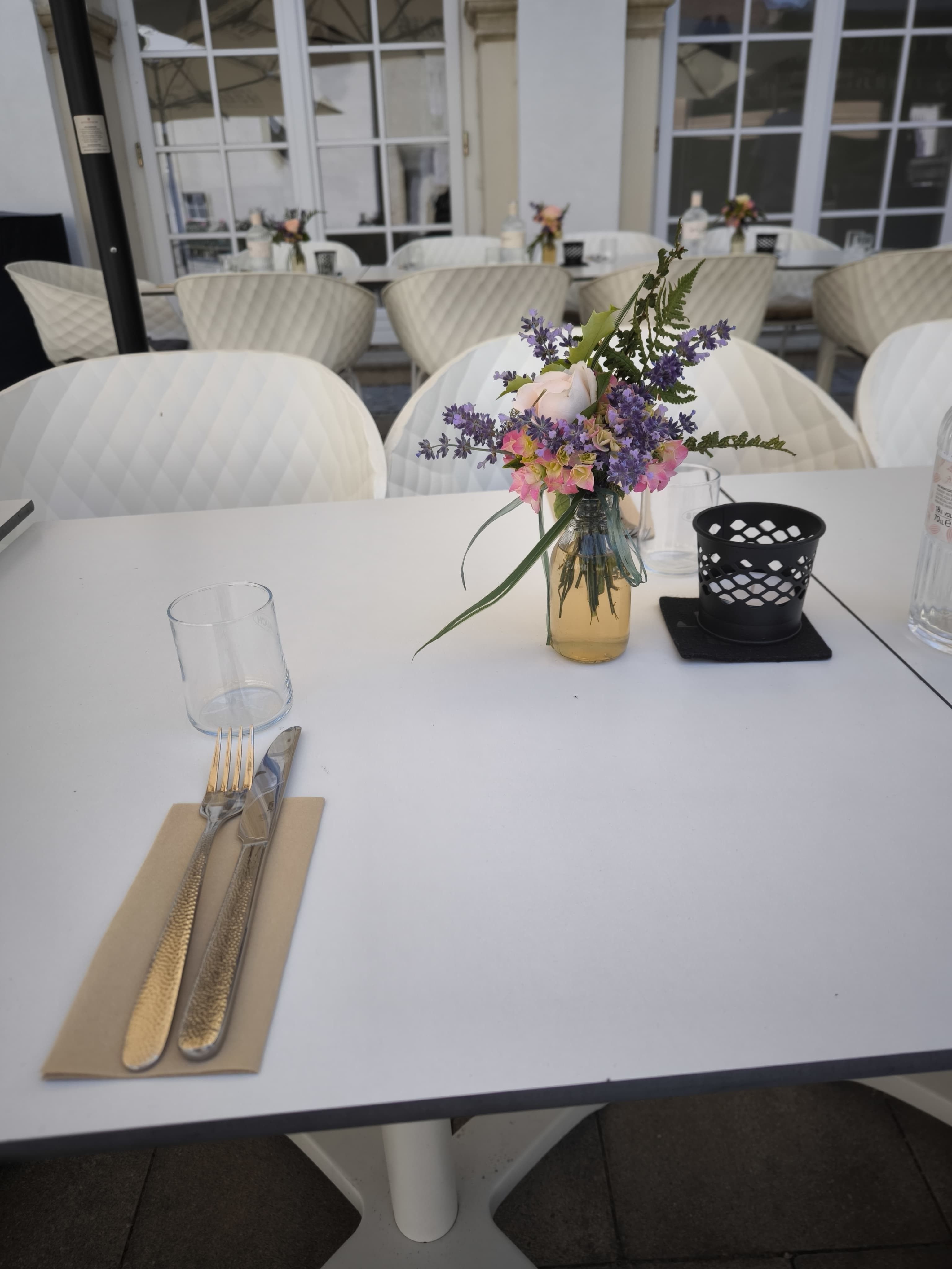 Terített asztal a teraszon, virágcsokorral és evőeszközökkel.