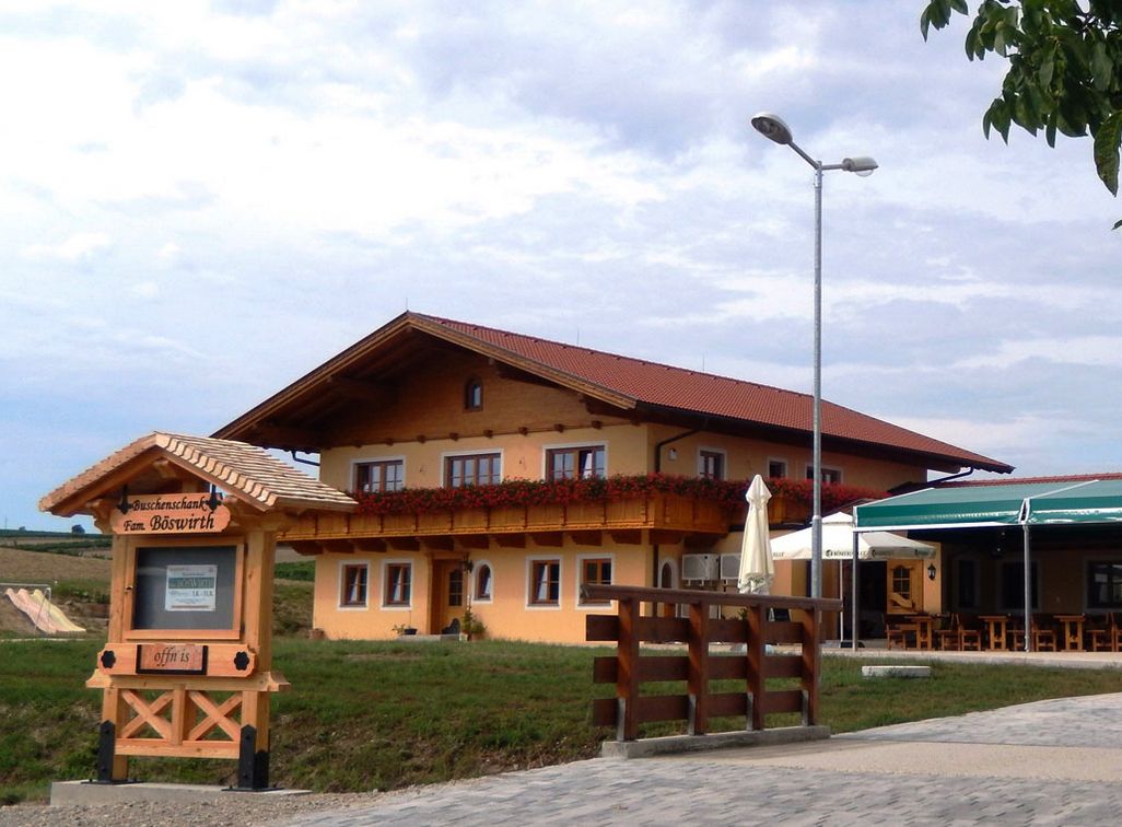 Hagyományos vendéglő, fából készült erkéllyel és virágdíszítéssel, a "Hagyományos borozó Fam. Böswirth" feliratú tábla mellett.