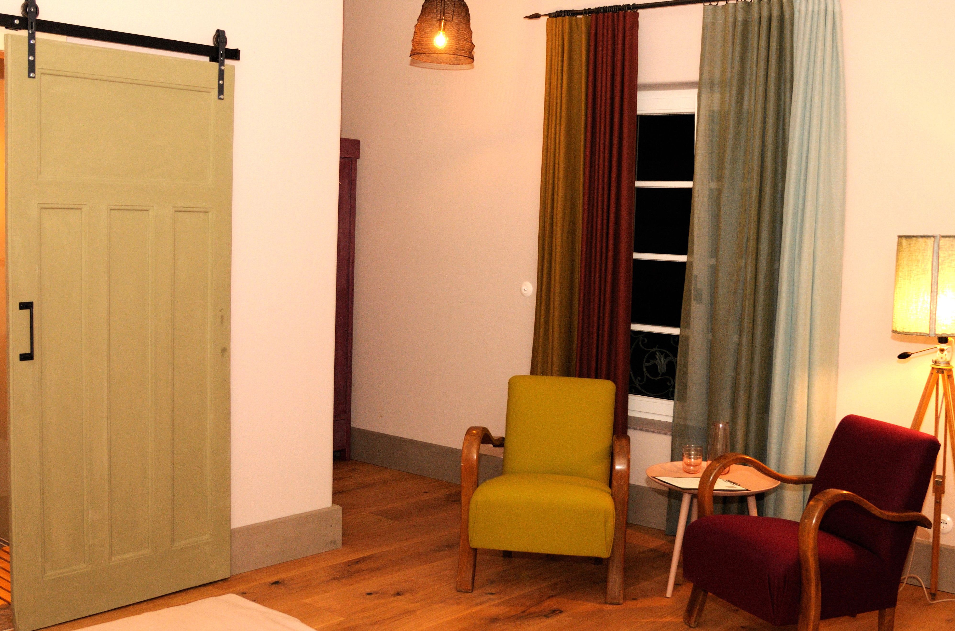 Hangulatos szoba, két fotel, egy kis asztal és egy lámpa. Egy tolóajtó és színes függönyök is láthatók.