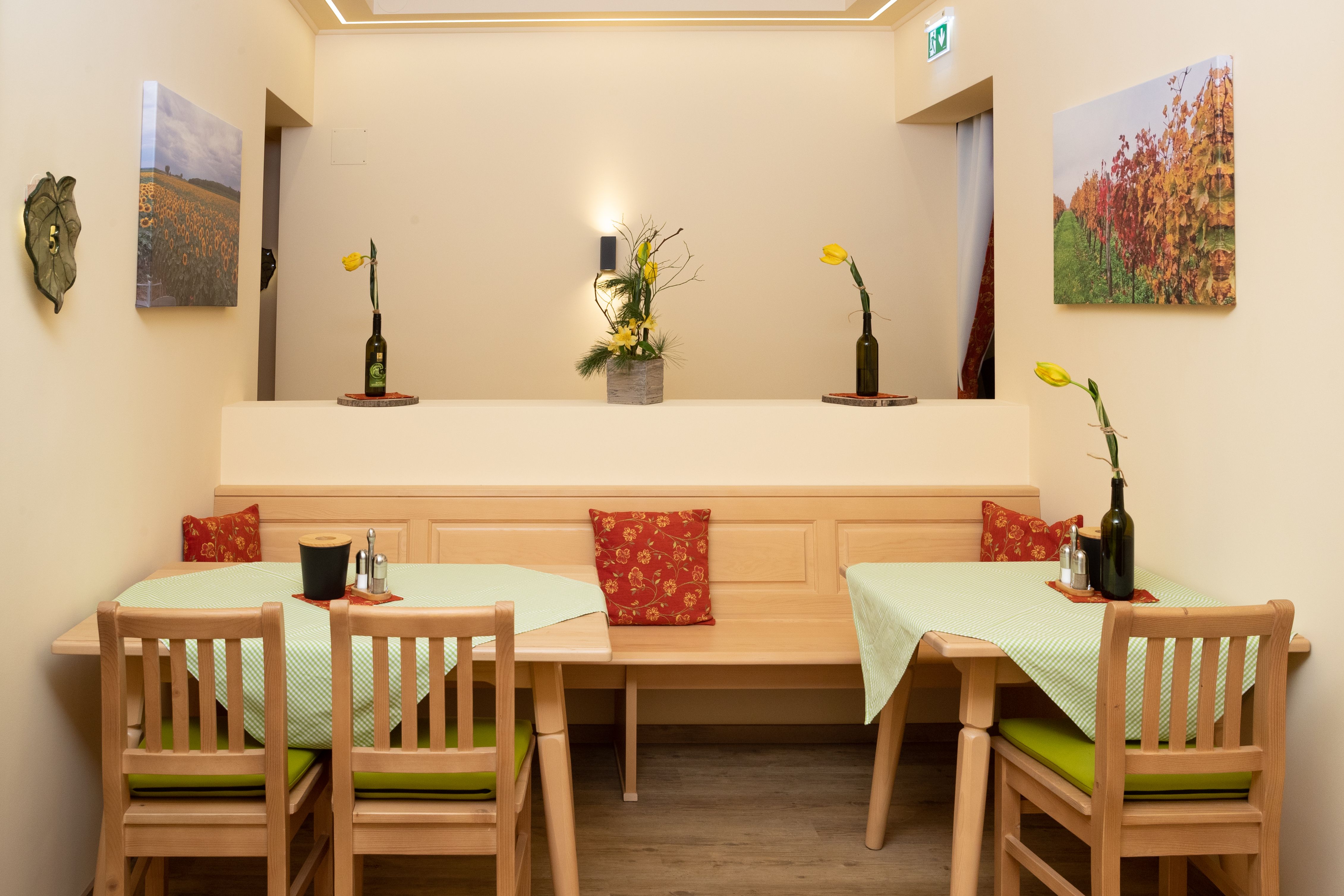 Hangulatos reggelizőterem, fabútorokkal, zöld terítőkkel és sárga virágokkal az üvegvázákban. A falakon tájképfestmények lógnak.