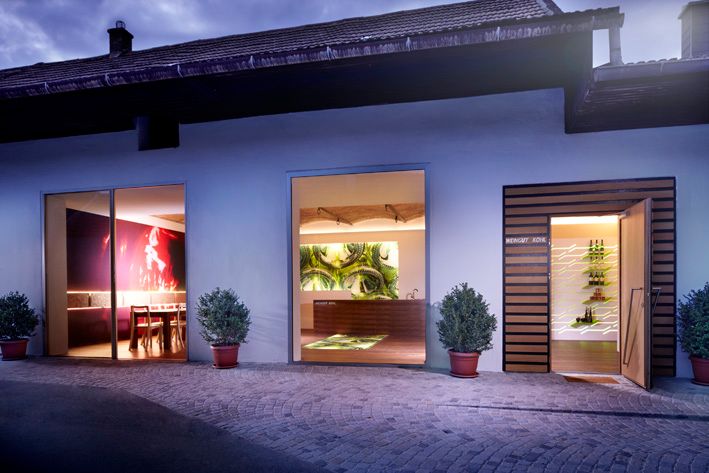 Egy modern borászat külső nézete kivilágított ablakokkal és növényekkel.