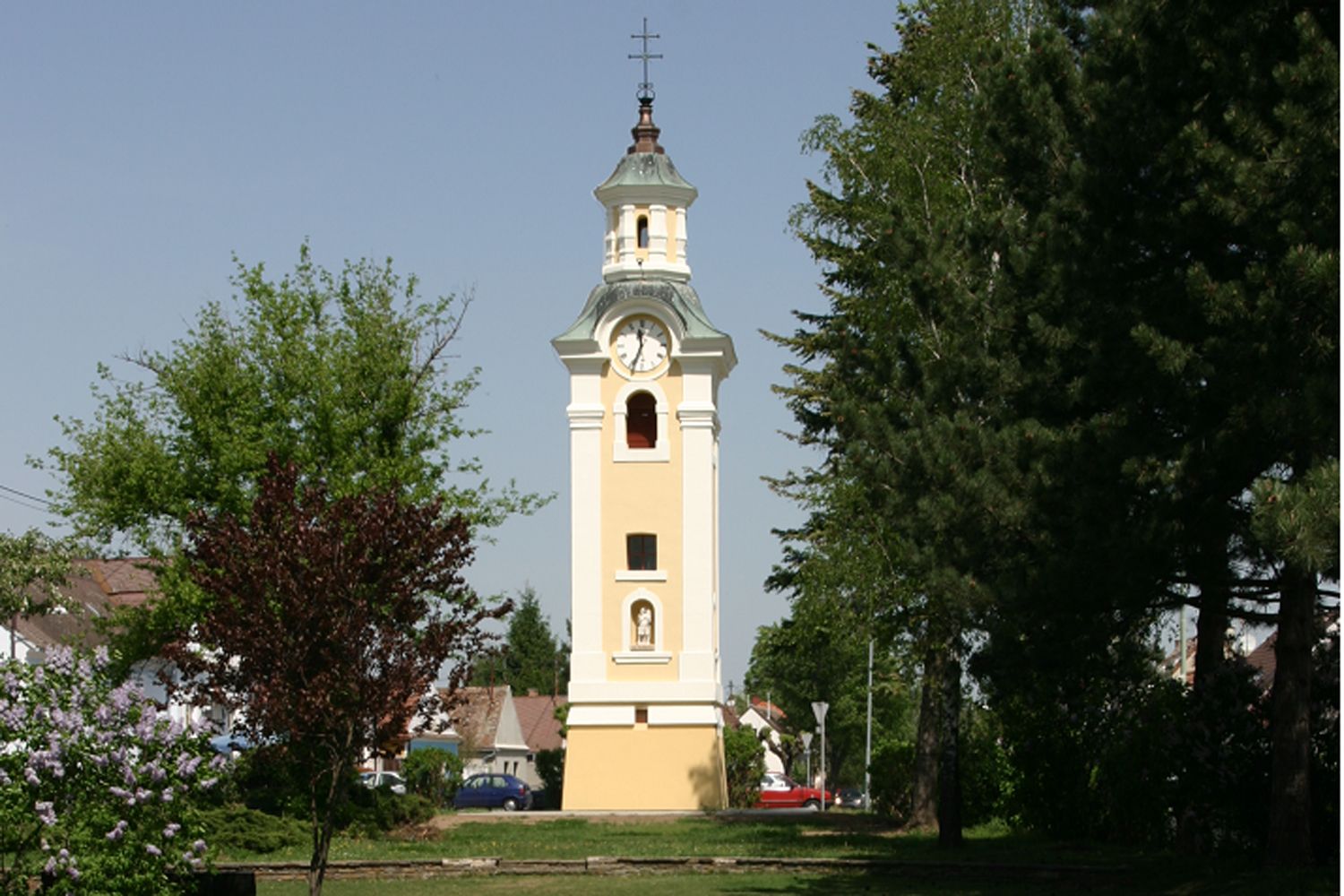 Sárga templomtorony órával Hohenauban, fákkal körülvéve.