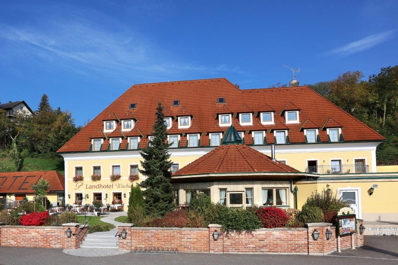 Külső nézet egy sárga vidéki hotelről, piros tetővel és kerttel.