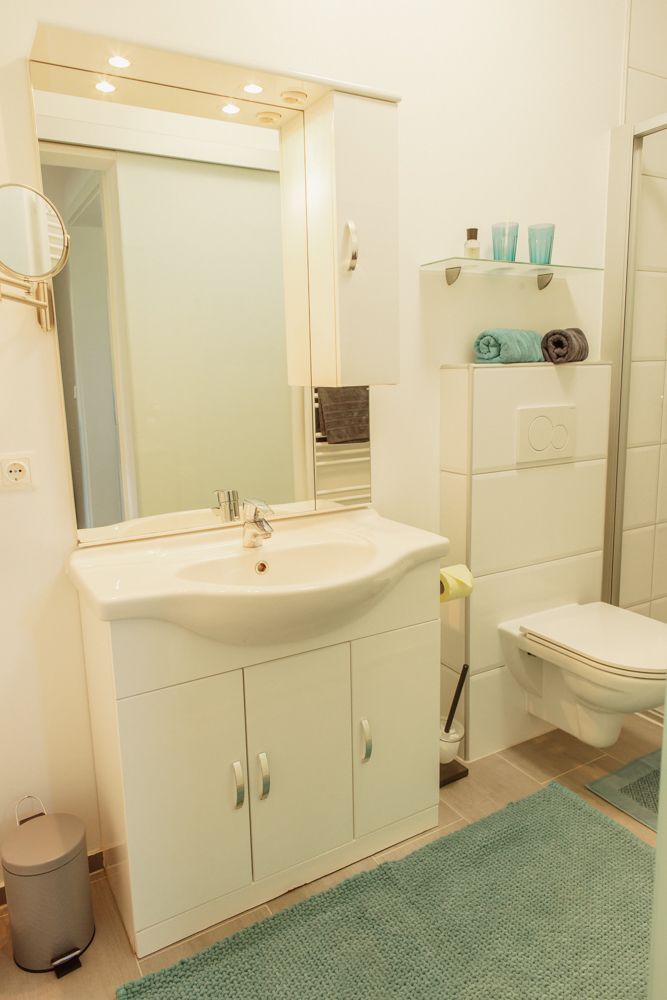 Modern fürdőszoba mosdóval, tükörrel, WC-vel és polcokkal.