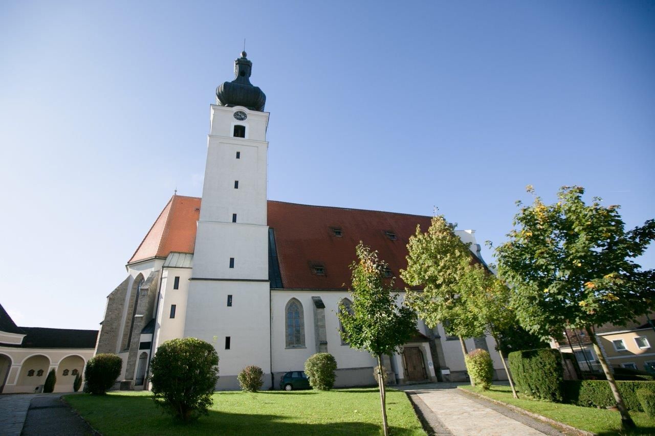 Mank zarándoktemplom toronnyal és vörös tetővel, fákkal és pázsittal körülvéve.
