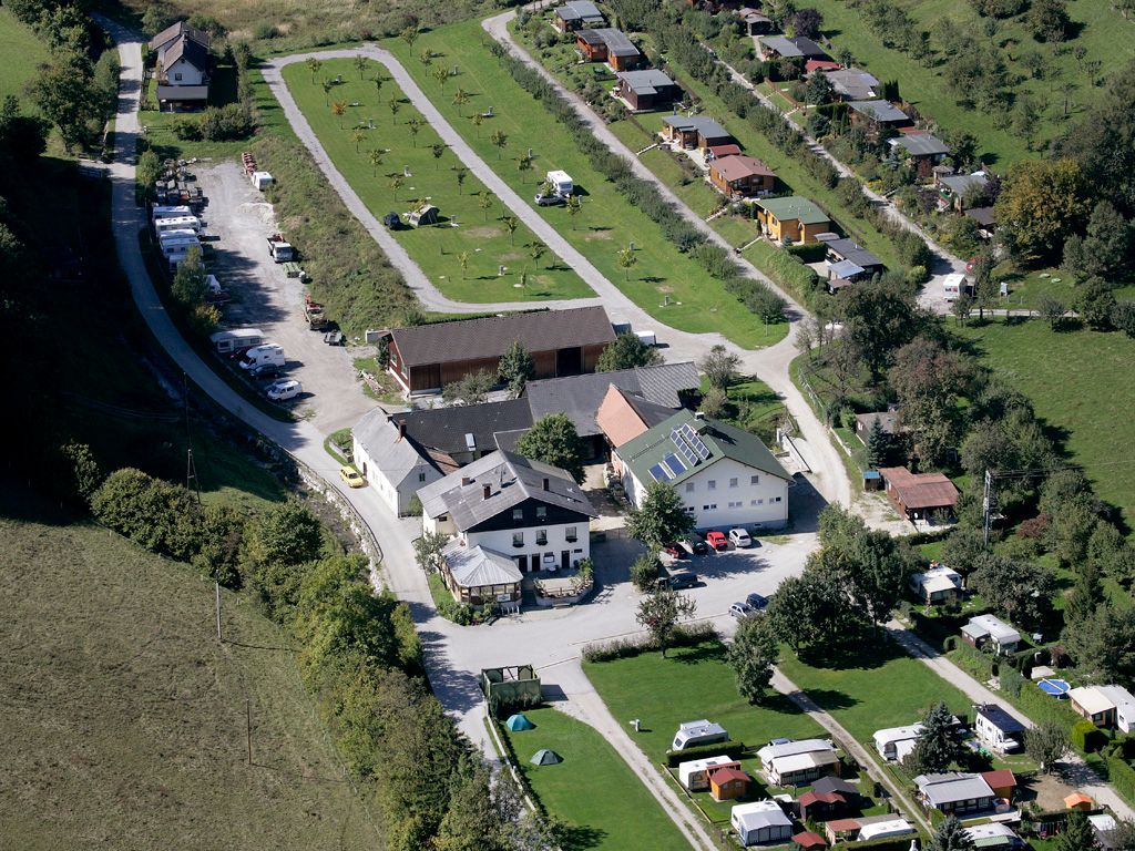 Légi felvétel egy kempingről, lakókocsikkal és épületekkel egy zöld tájban.