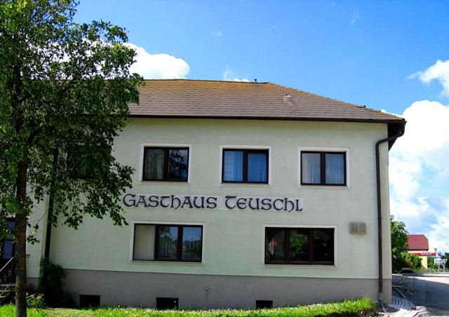 A Teuschl fogadó külső nézete fákkal és kék éggel.