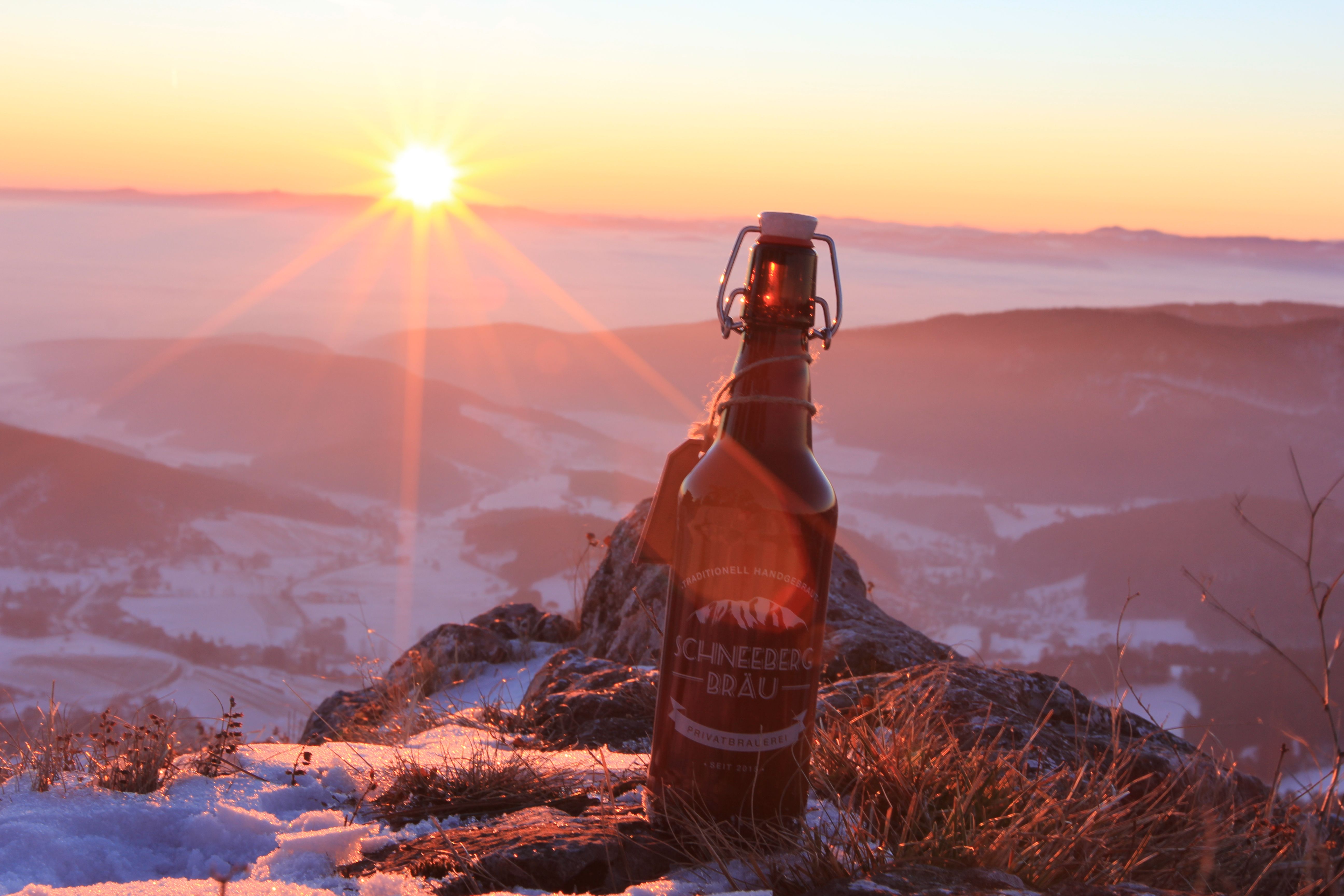 Egy üveg Schneeberg Bräu sör áll egy hófödte hegyen naplementekor.