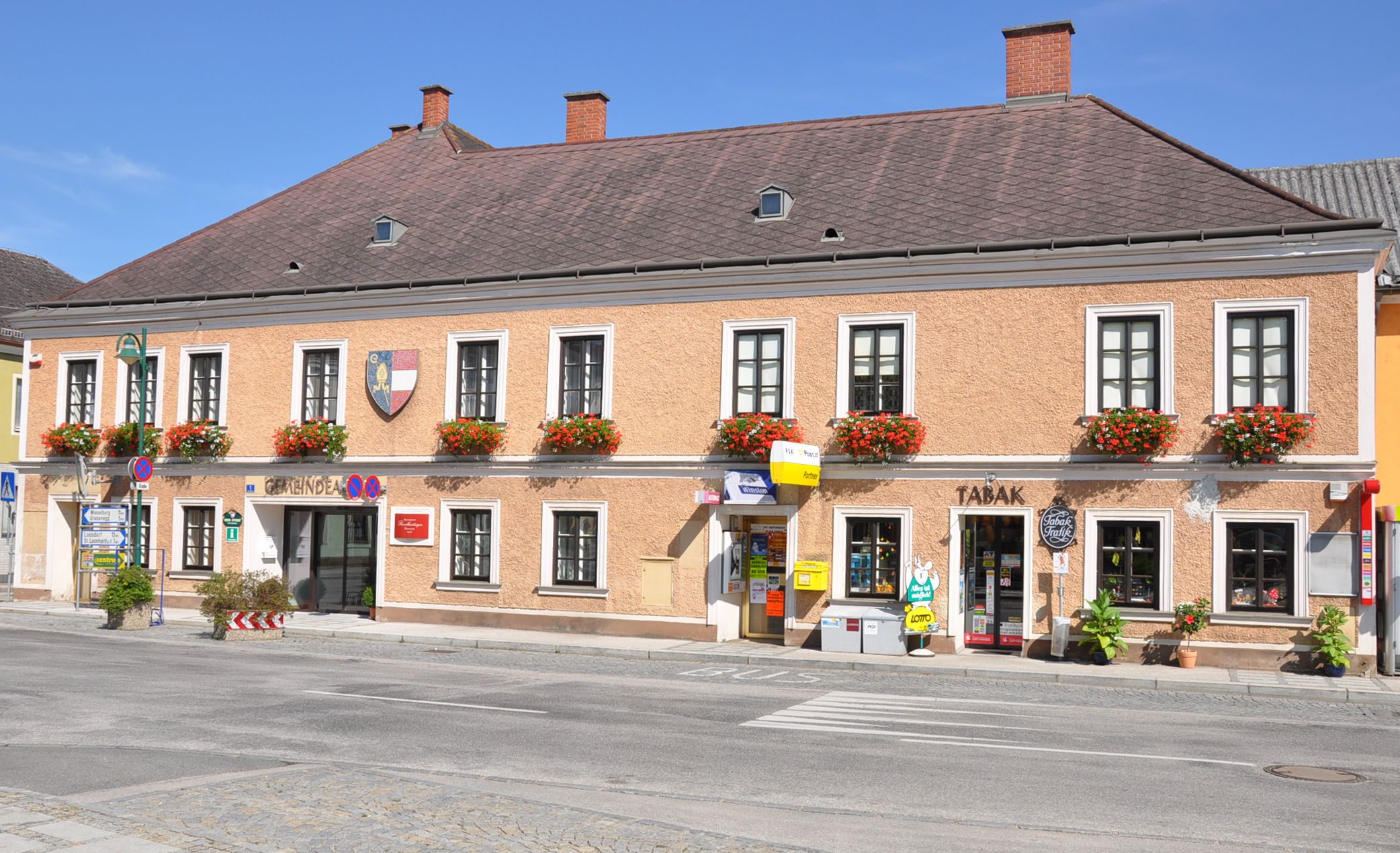 Kétszintes épület, virágokkal az ablakokban és üzletekkel a földszinten Ruprechtshofenben.