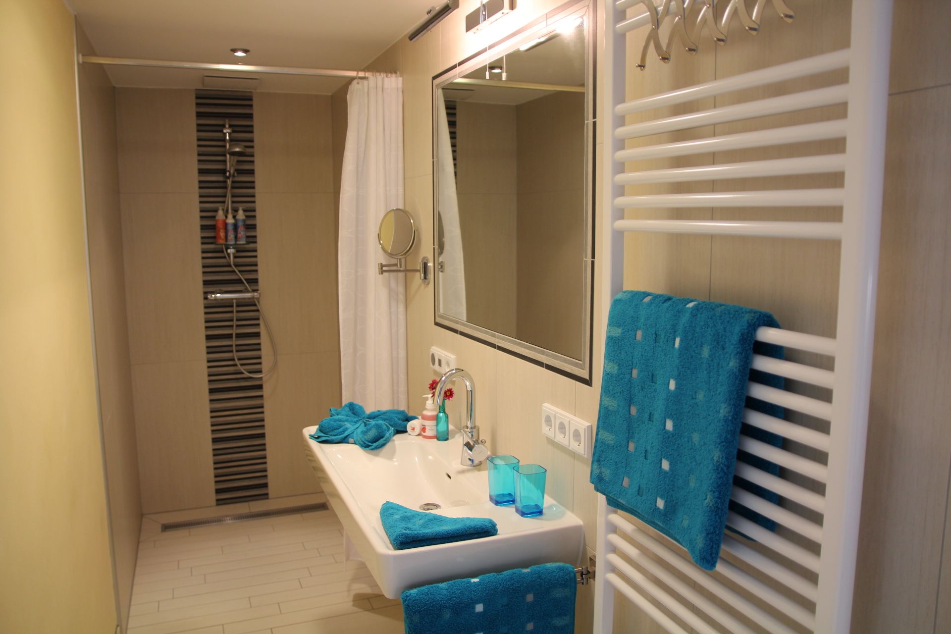 Modern fürdőszoba zuhanyzóval, mosdókagylóval és kék törölközőkkel.