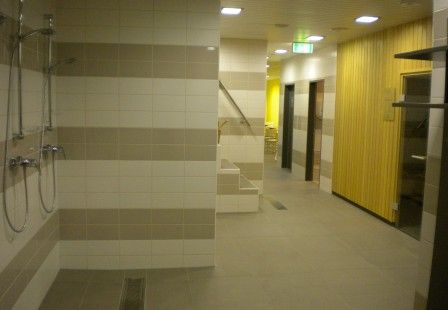 Belső nézet egy szaunaterületről, zuhanyzókkal és fából készült falakkal.