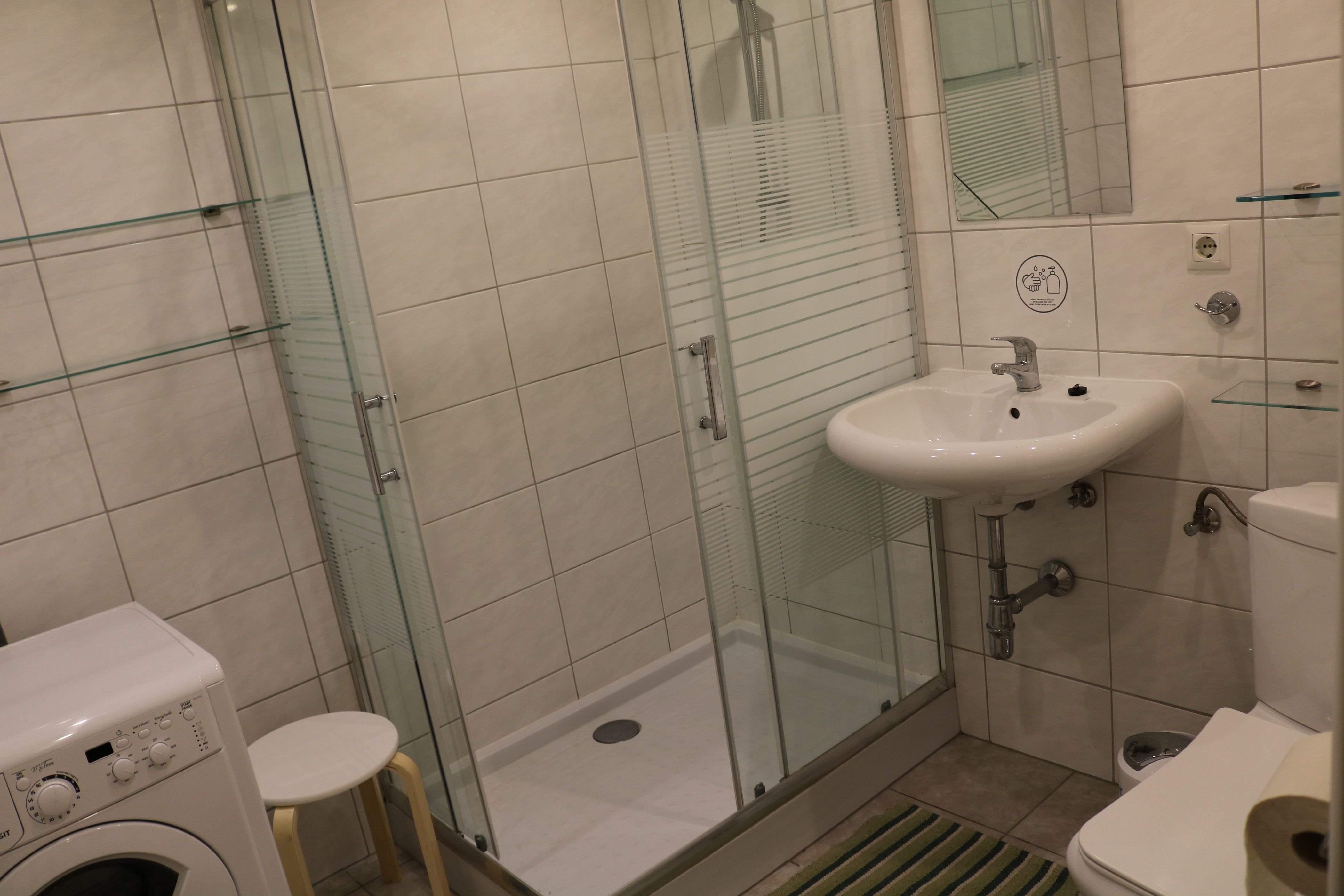 Modern fürdőszoba zuhanyzóval, mosdóval, WC-vel és mosógéppel.