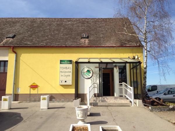 Sárga épület "Tomba's Heurigenschenke" felirattal. Bejárat lépcsővel és üvegtetővel.
