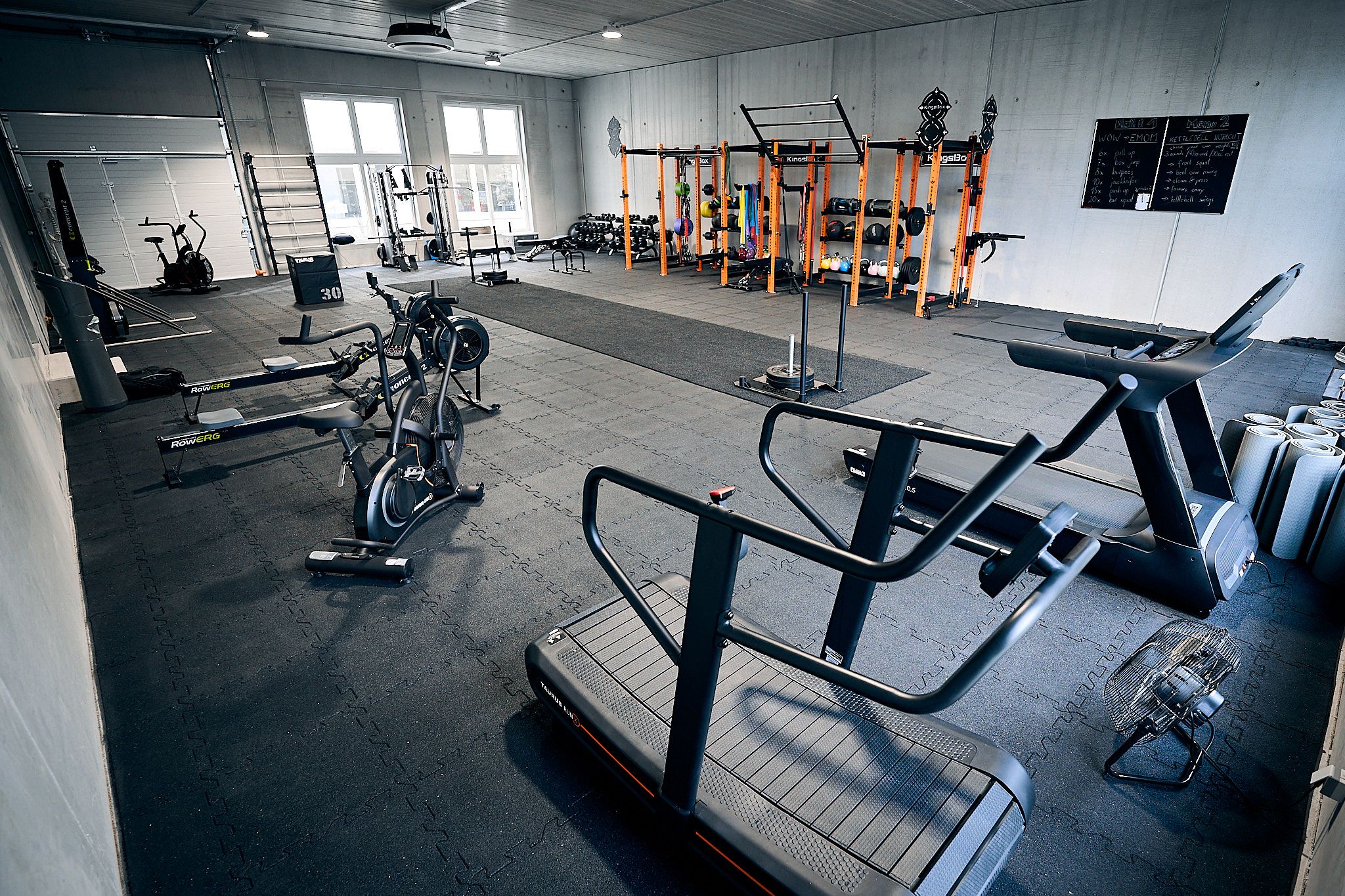 Egy fitneszterem belső nézete különböző edzőeszközökkel, például futópadokkal, kerékpárokkal és súlyzókkal.