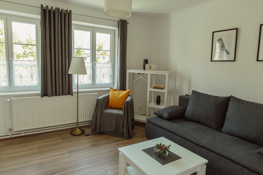 Világos nappali szürke kanapéval, karosszékkel, állólámpával és fehér bútorokkal.