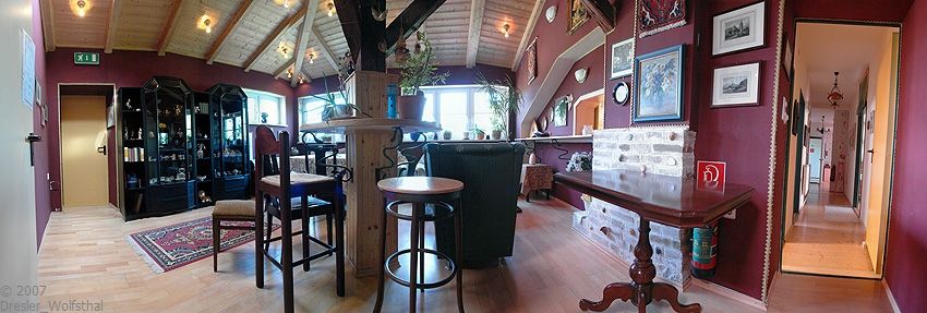 Hangulatos klubhelyiség fabútorokkal, szőnyeggel és képekkel a falakon.