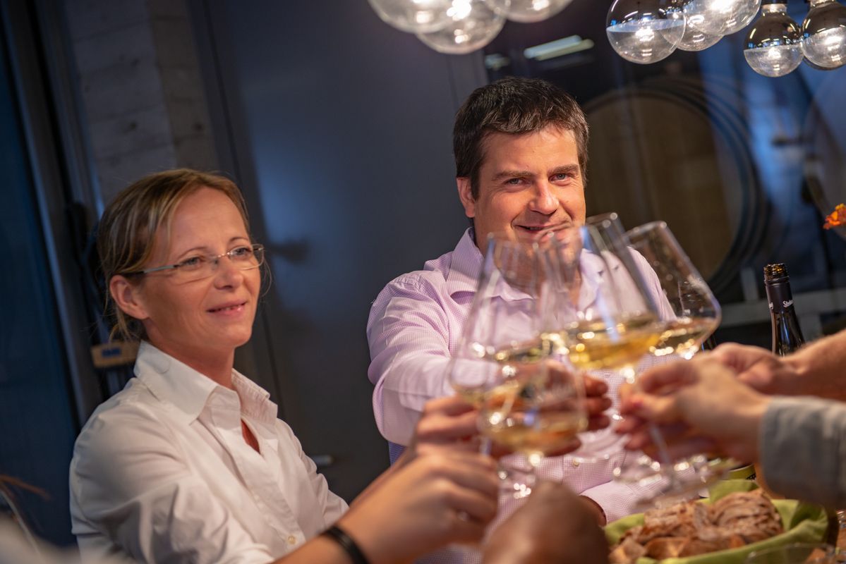 Az emberek egy asztalnál koccintanak a borospoharakkal.