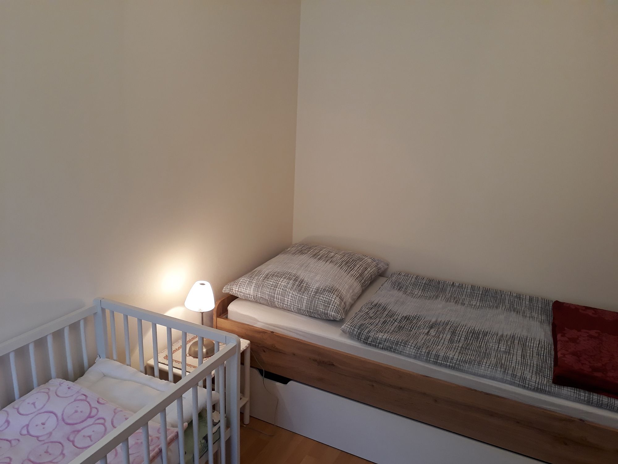 Egyágyas szoba egyszemélyes ággyal, kisággyal és éjjeli lámpával.